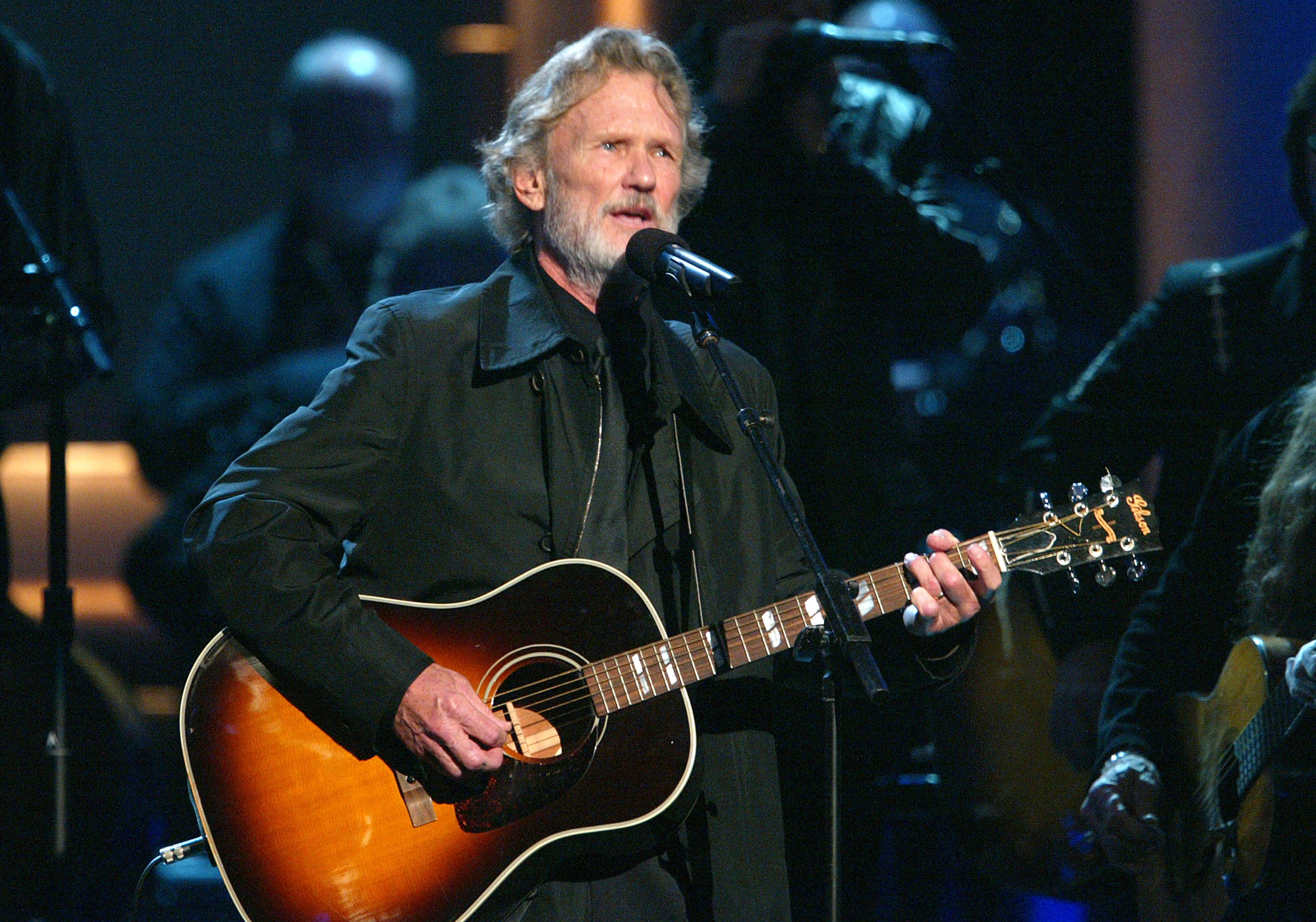 Kris Kristofferson, sunburst acoustic guitar, dimly lit stage, 2K Desktop Wallpaper