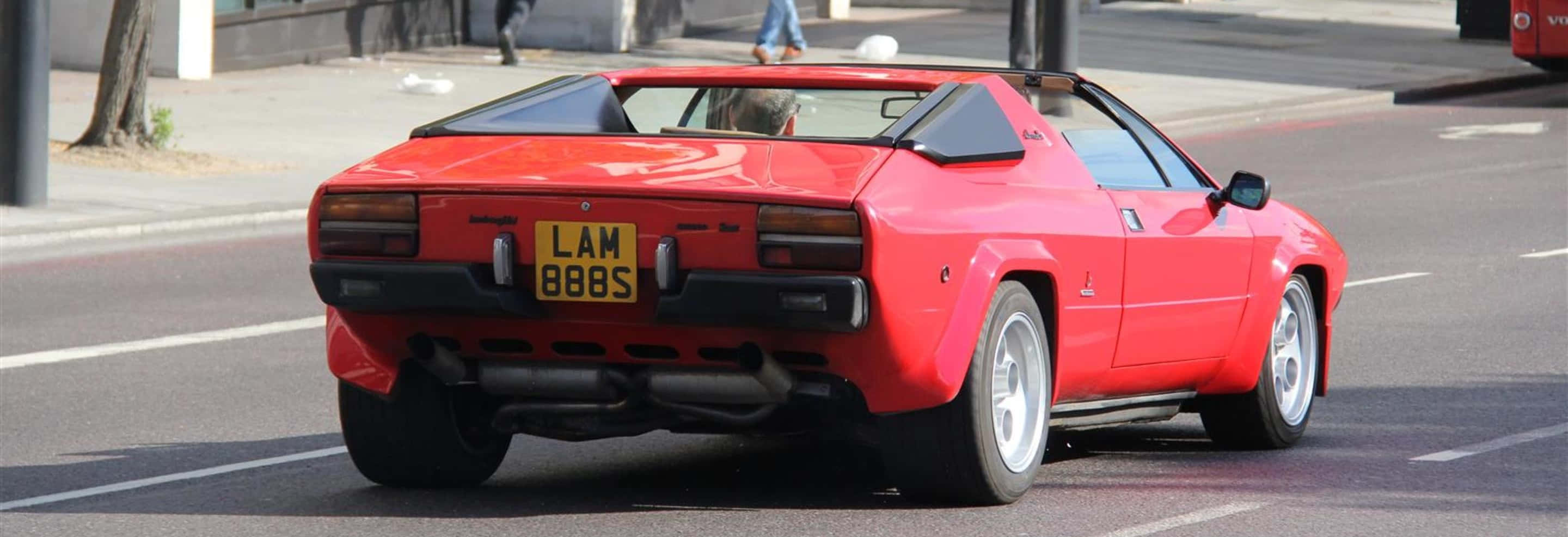 Lamborghini Urraco, vibrant red, sunlit city street, 2K Desktop Wallpaper