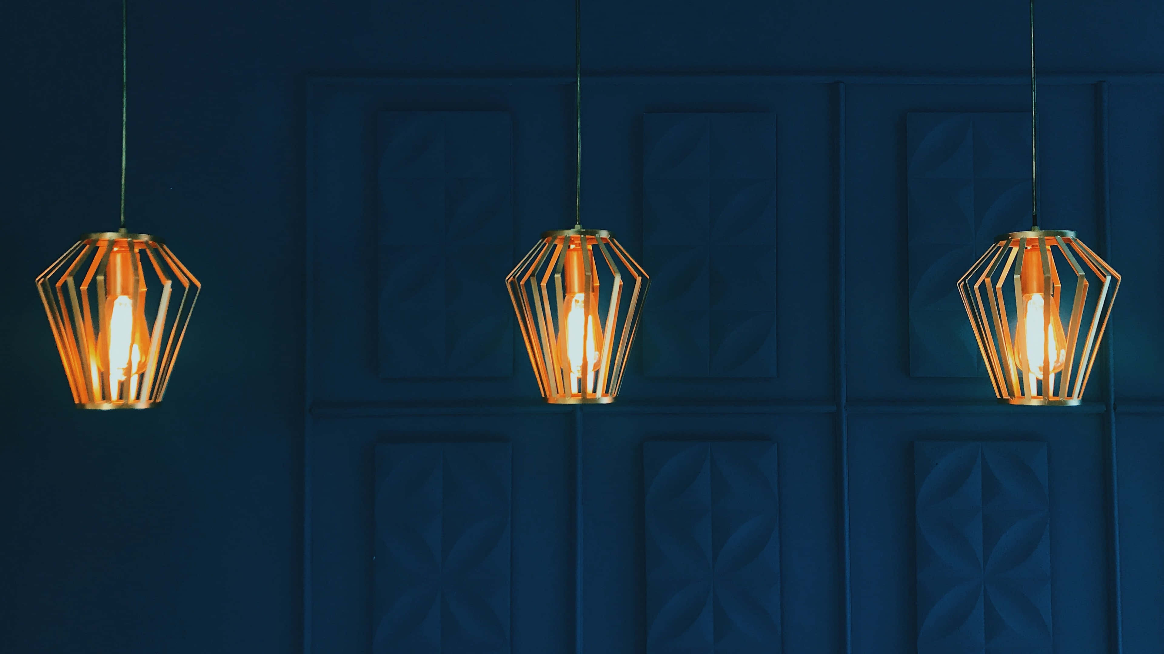 modern pendant lights, textured navy blue paneled wall, warm glow, 4K Desktop Wallpaper