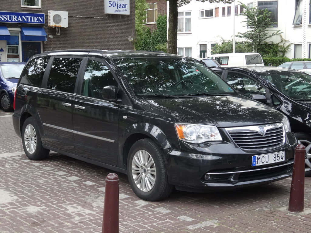 Lancia Voyager, sleek black minivan, brick-paved street, SD Desktop Wallpaper