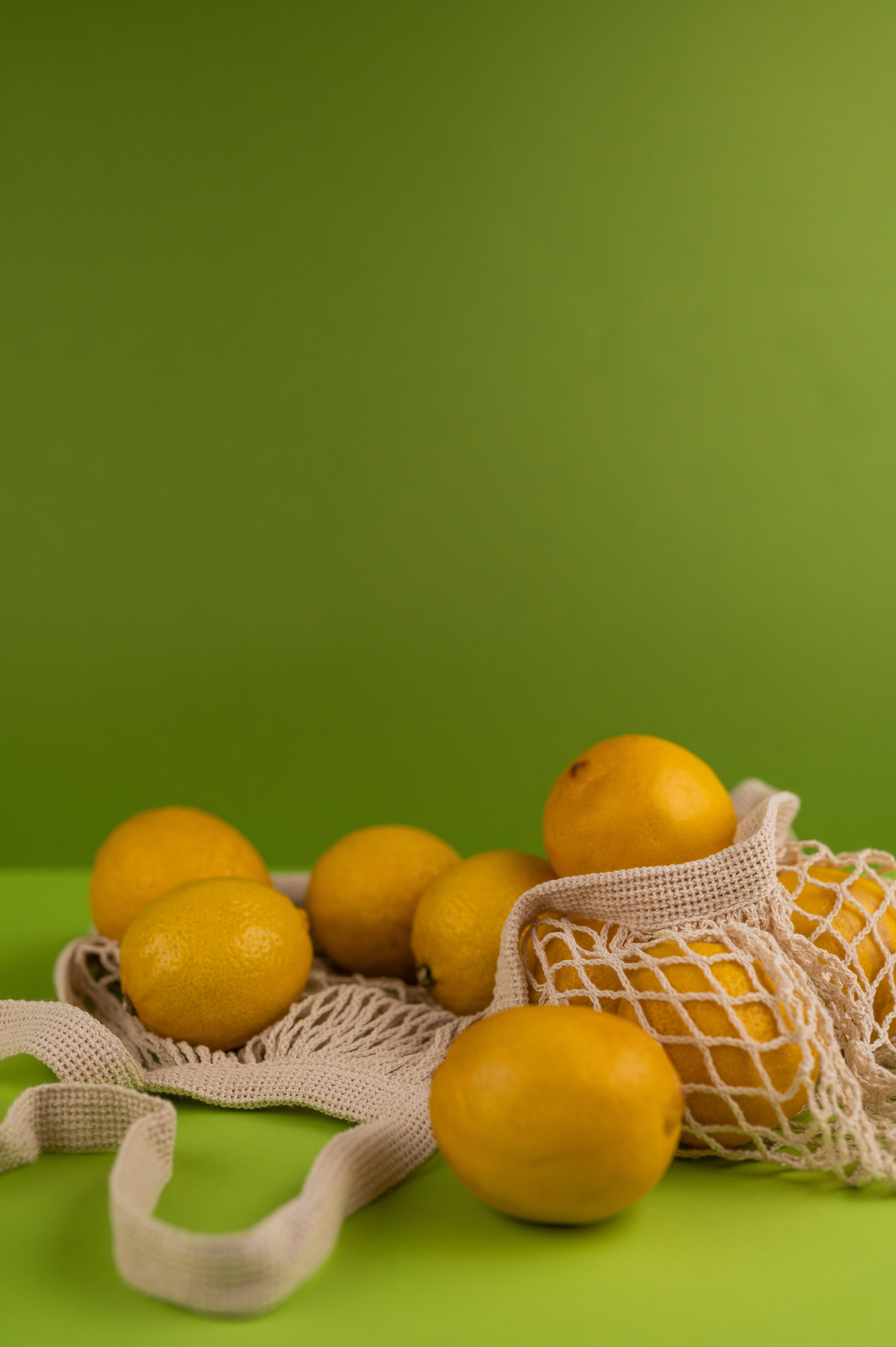 Fresh lemons, beige mesh bag, vibrant green background, 5K Phone Wallpaper