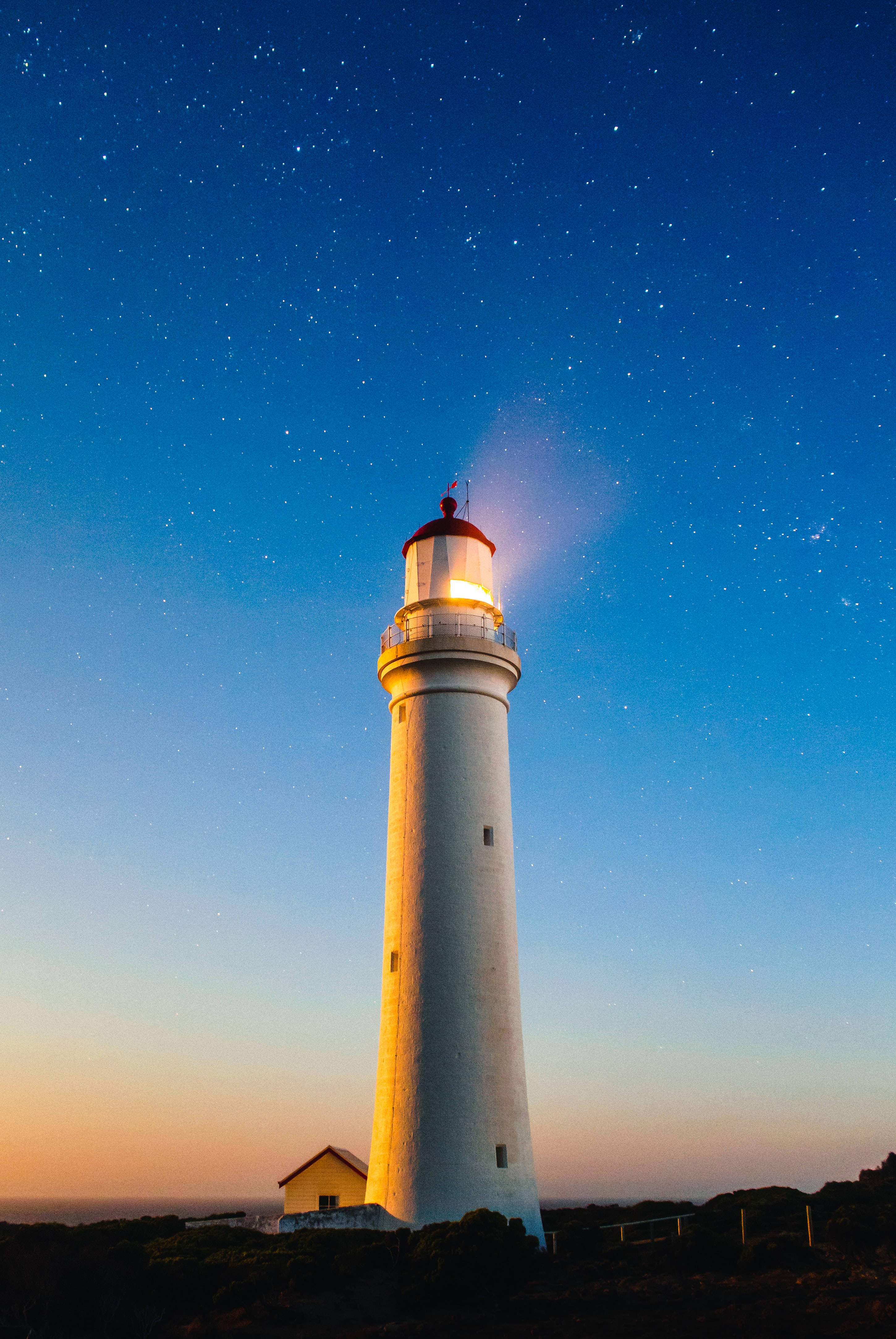 white lighthouse, starry twilight sky, gradient blue and orange hues, 4K Phone Wallpaper