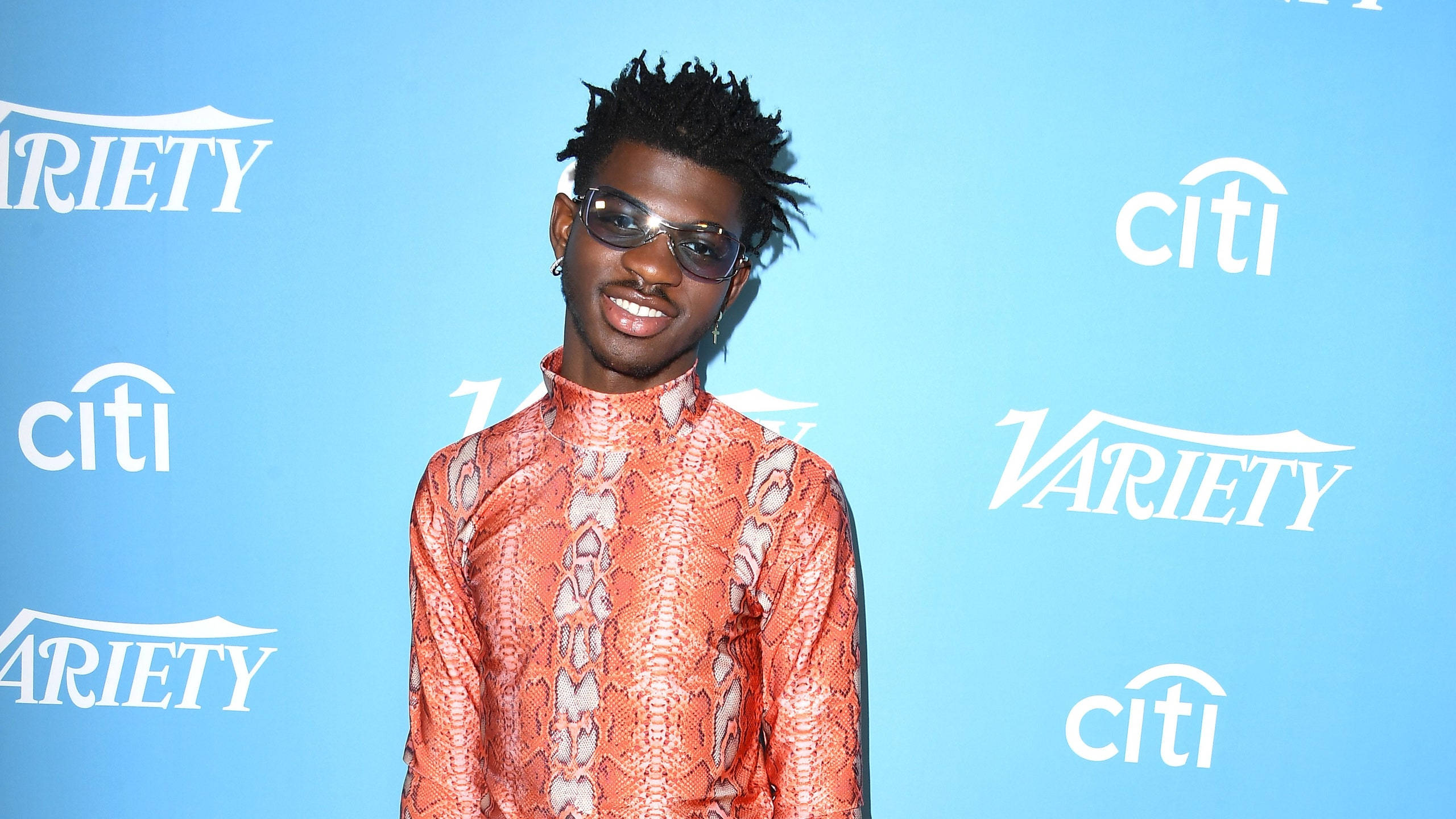 Lil Nas X, vibrant orange snakeskin shirt, blue branded backdrop, 2K Desktop Wallpaper