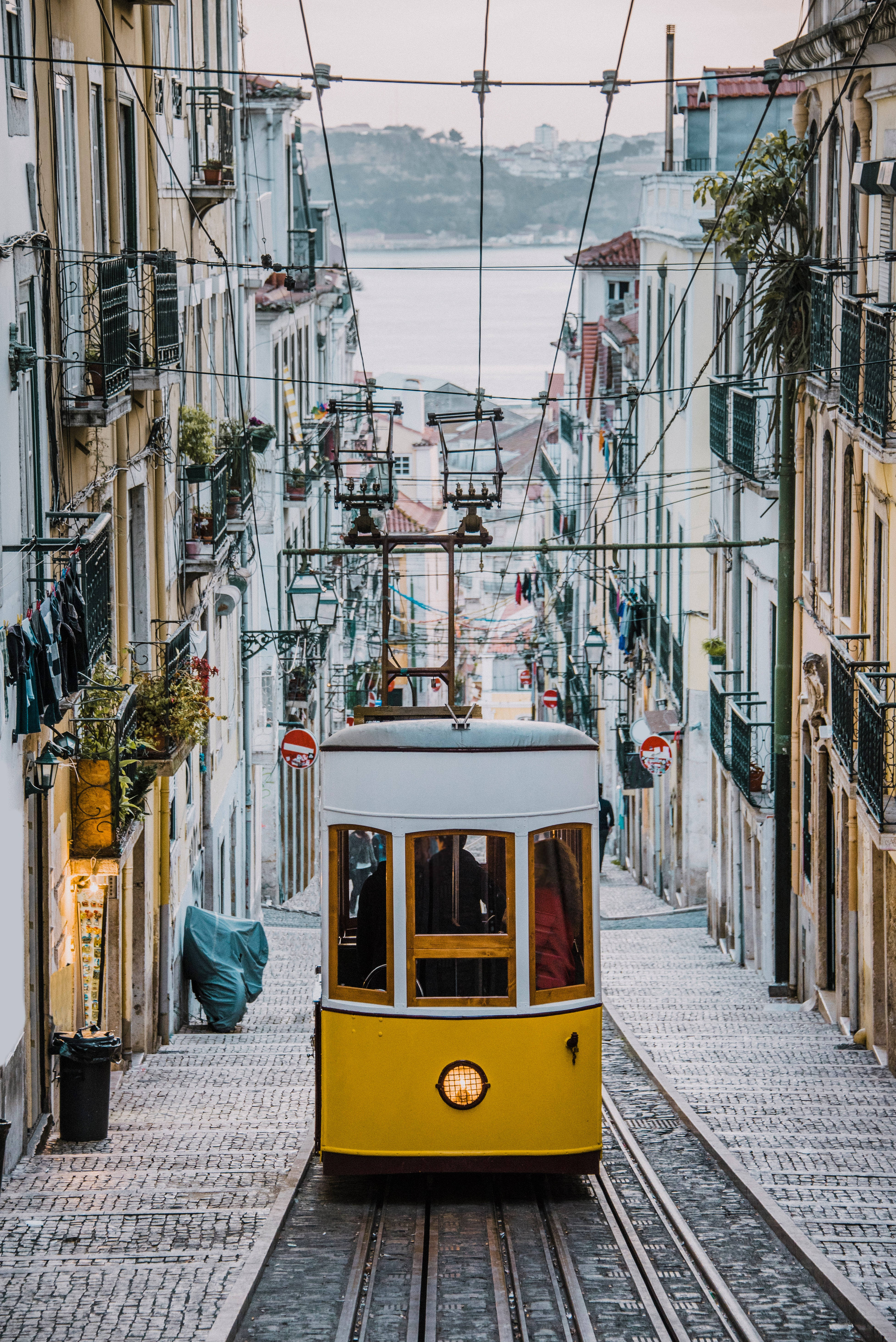 yellow tram, narrow cobblestone street, colorful European buildings, 5K Phone Wallpaper