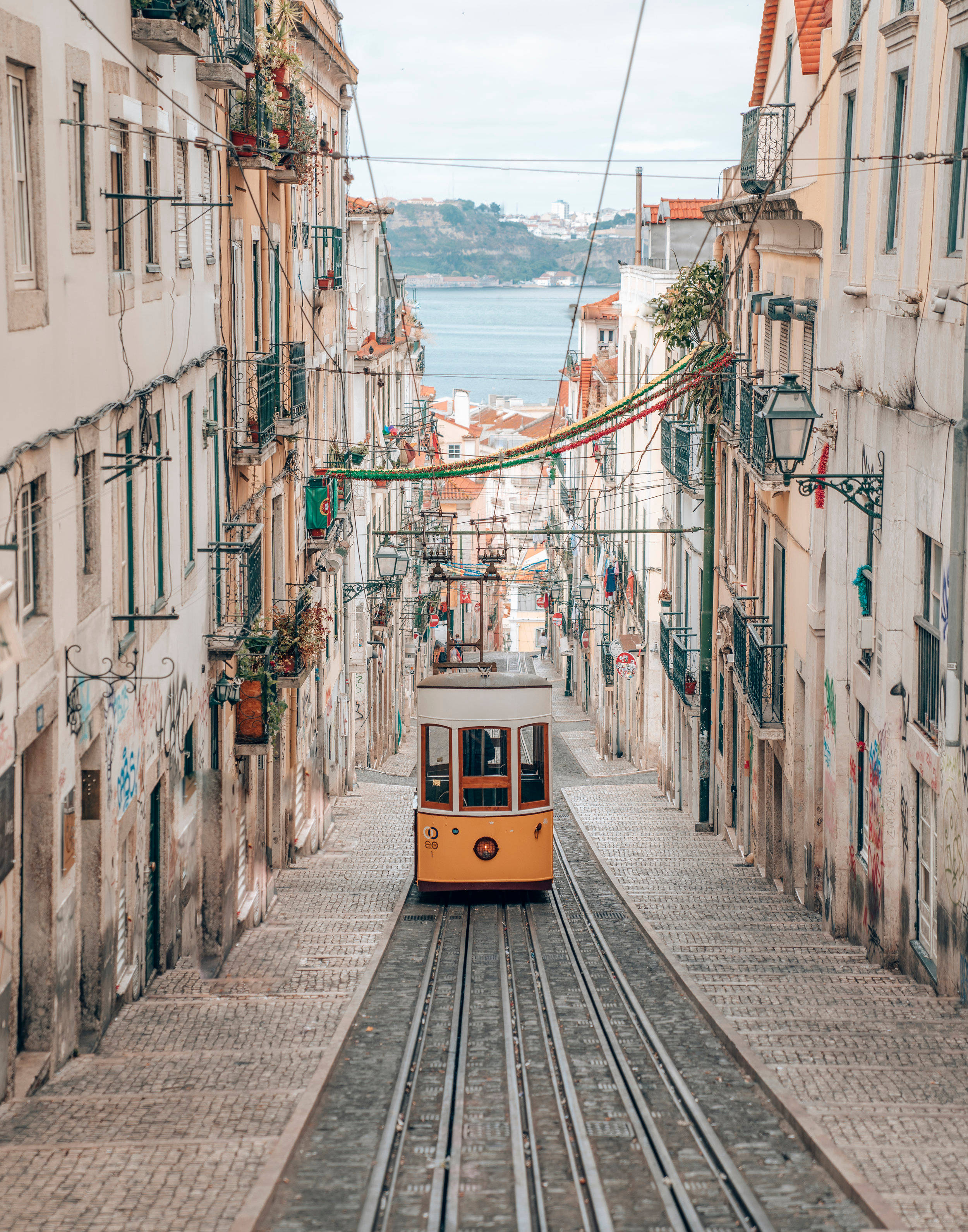 yellow tram, narrow cobblestone street, pastel buildings, 2K Phone Wallpaper