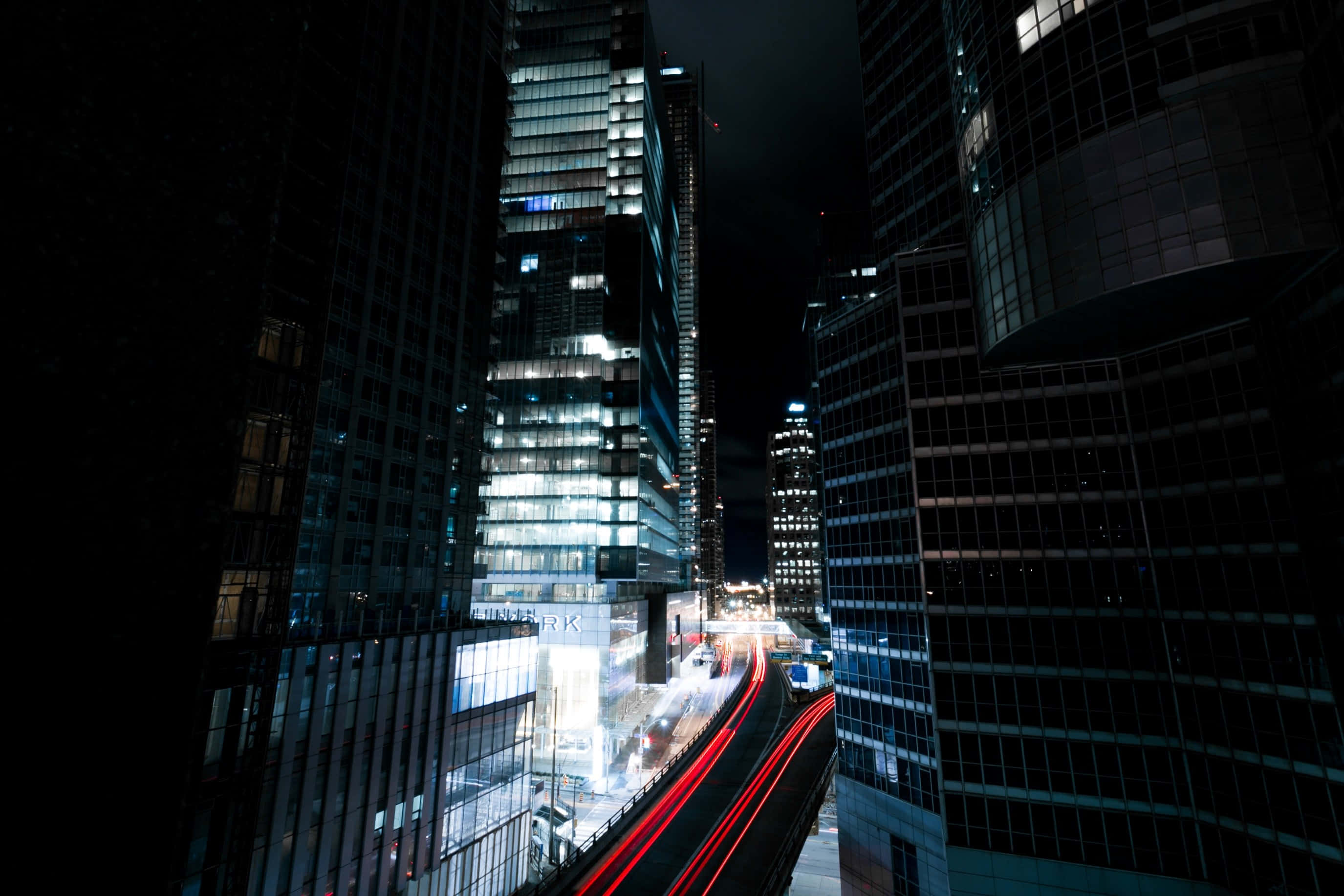 Lit iPhone, nighttime cityscape, towering glass skyscrapers, 2K Desktop Wallpaper
