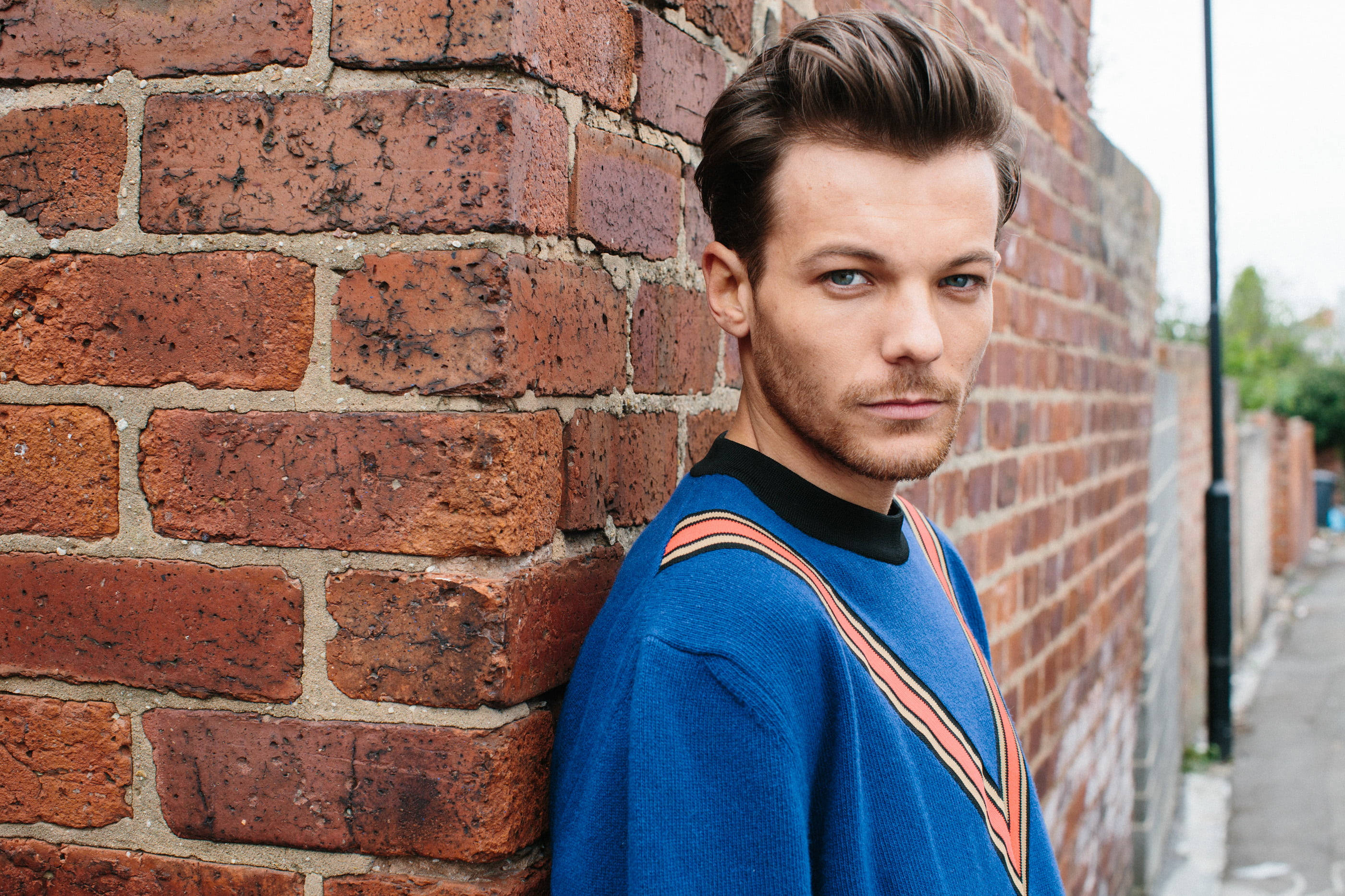 Louis Tomlinson, blue sweater, weathered red brick wall, 2K Desktop Wallpaper