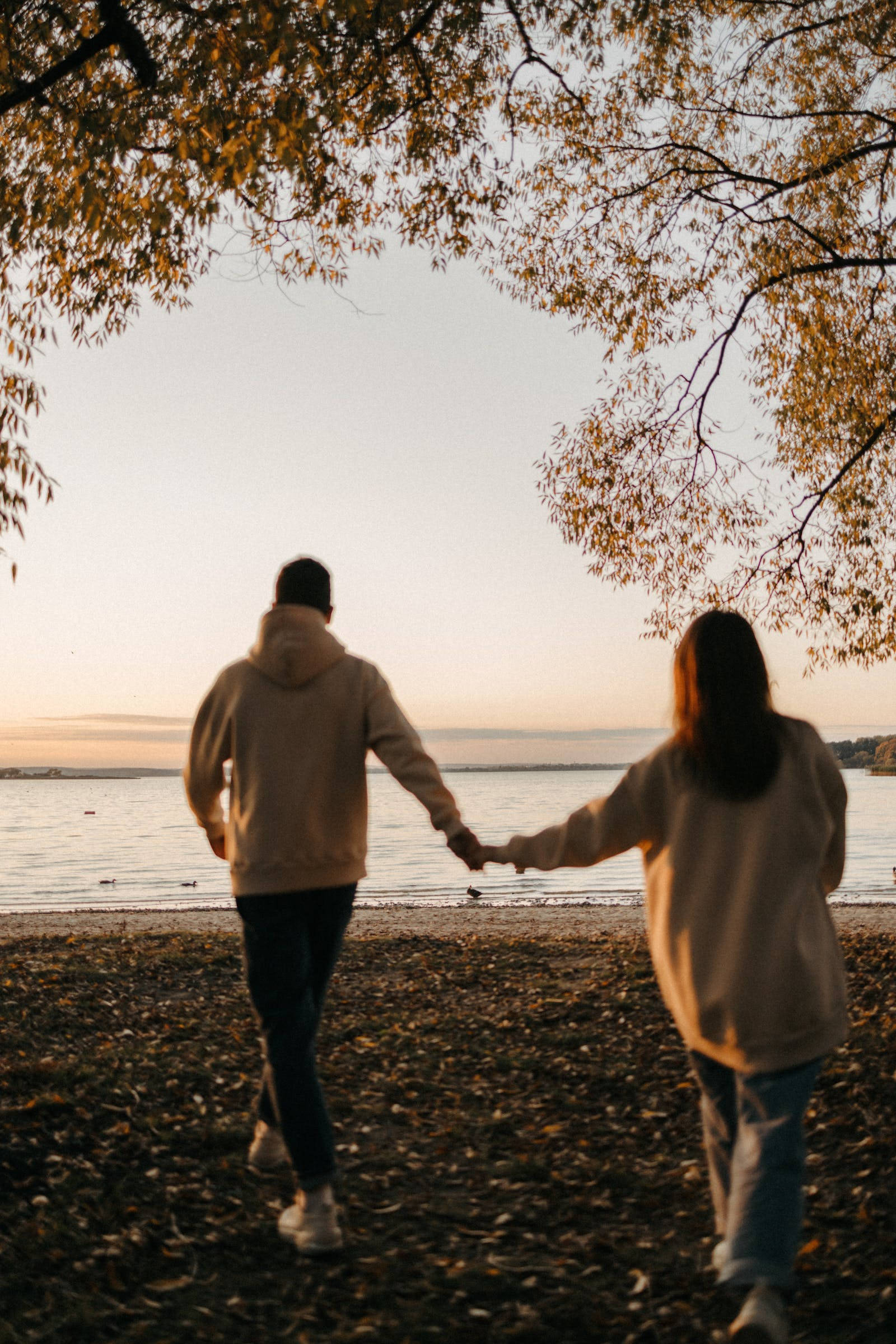 couple, leaf-strewn shore, golden autumn trees, Full HD Phone Wallpaper