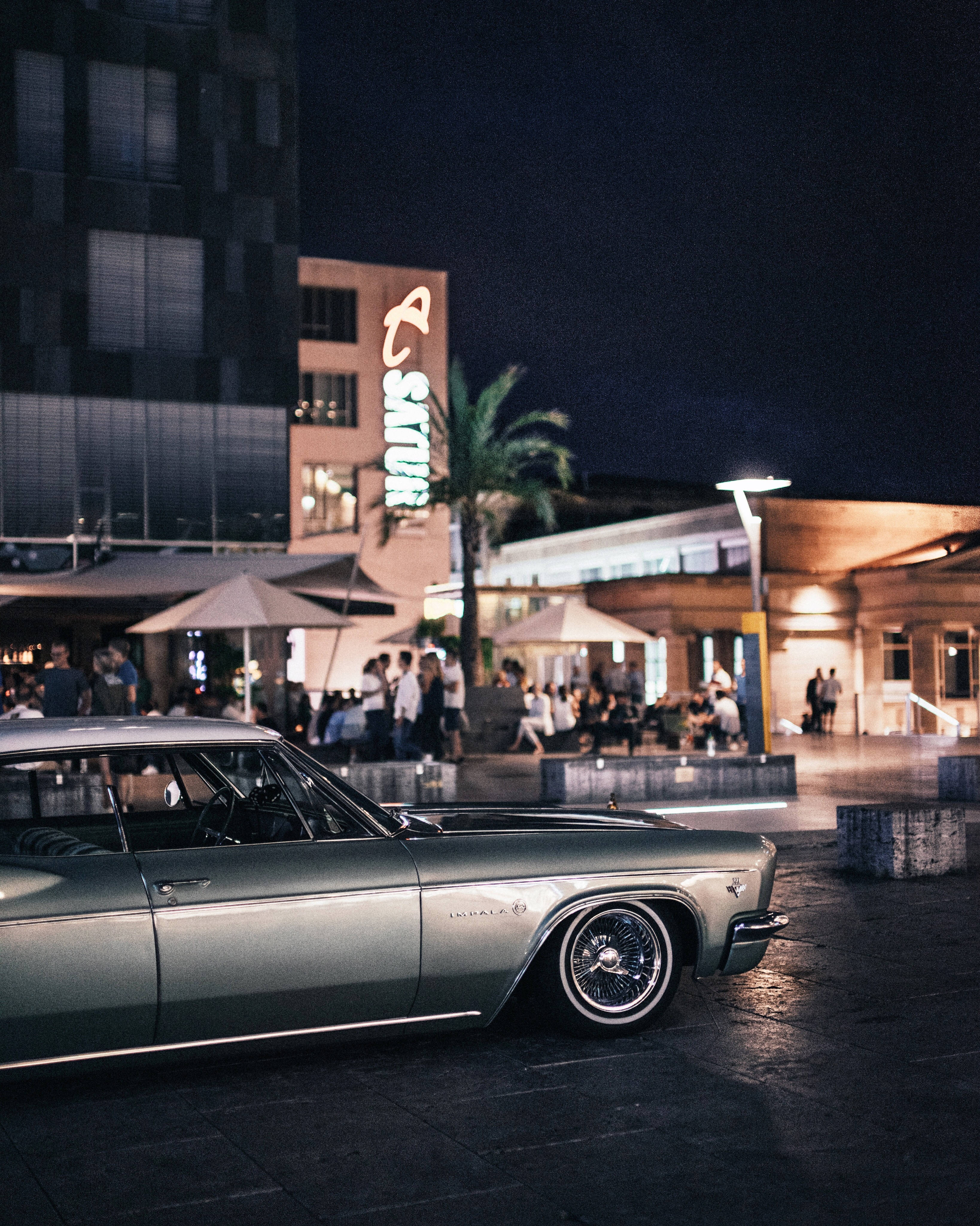 1965 Silver Impala, neon lights, bustling urban plaza, 4K Phone Wallpaper