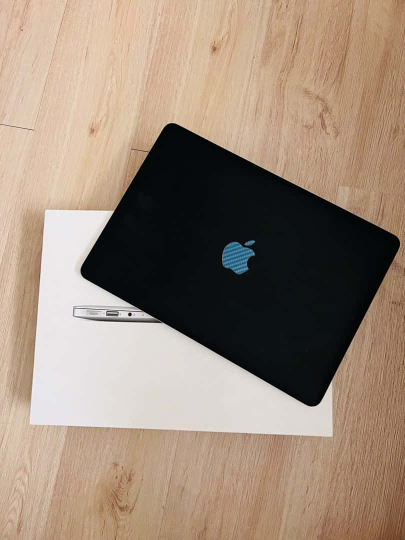 black MacBook, blue textured Apple logo, white desk, SD Phone Wallpaper
