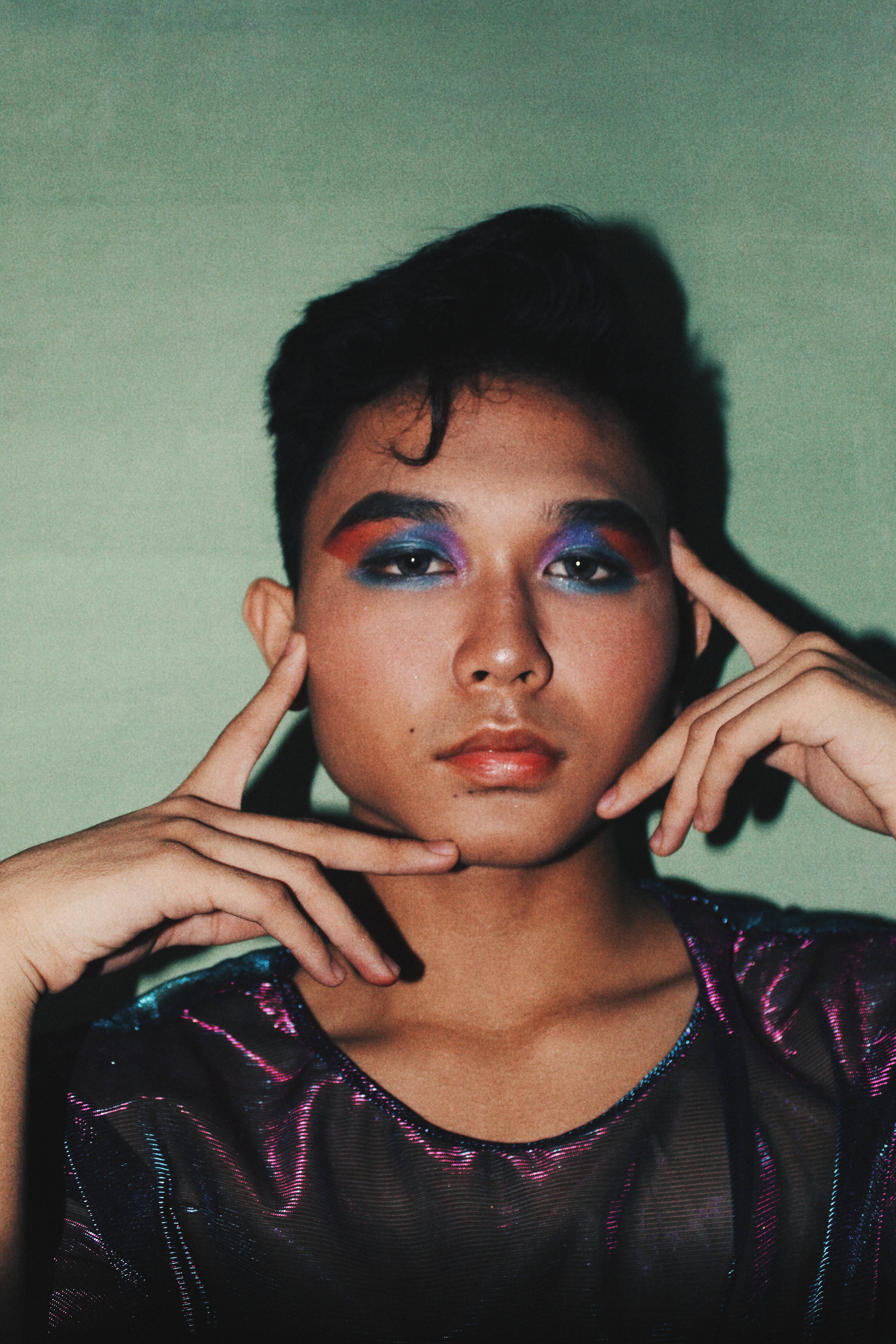 rainbow eyeshadow, finger tips on temples, muted green wall, 5K Phone Wallpaper
