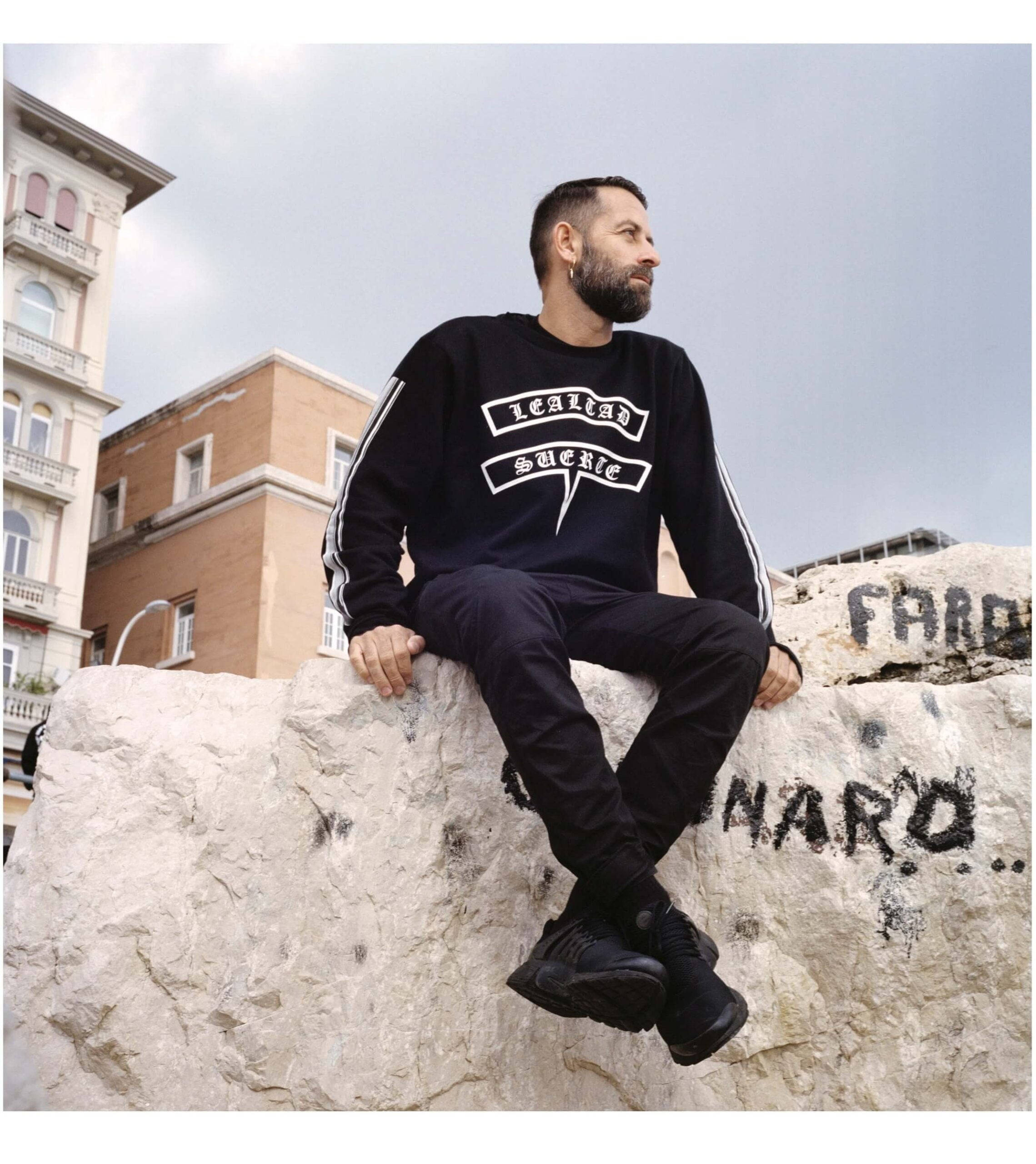 Marcelo Burlon, black sweatshirt, graffiti-marked stone wall, 2K Phone Wallpaper
