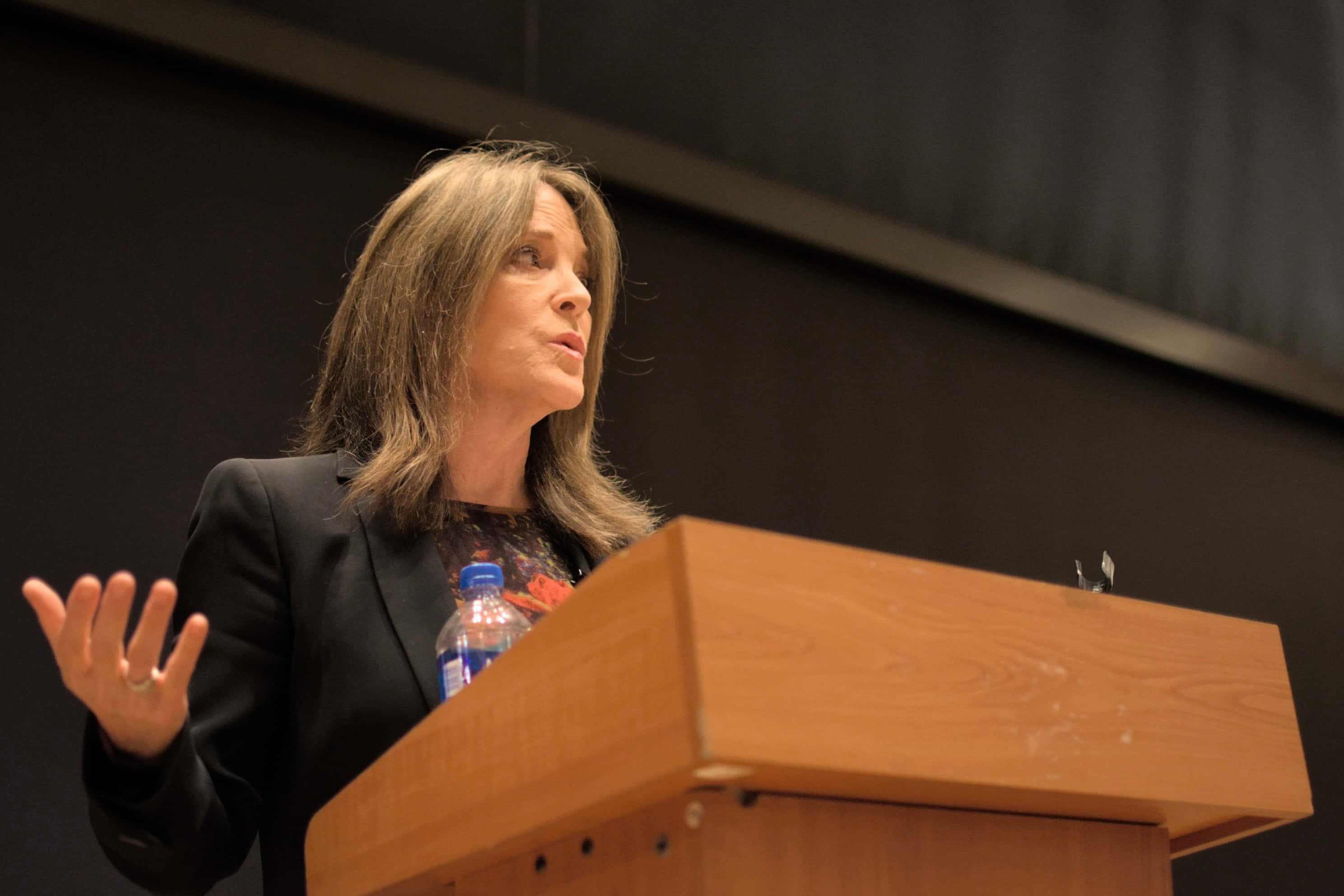 Marianne Williamson, black blazer, wooden podium, 2K Desktop Wallpaper