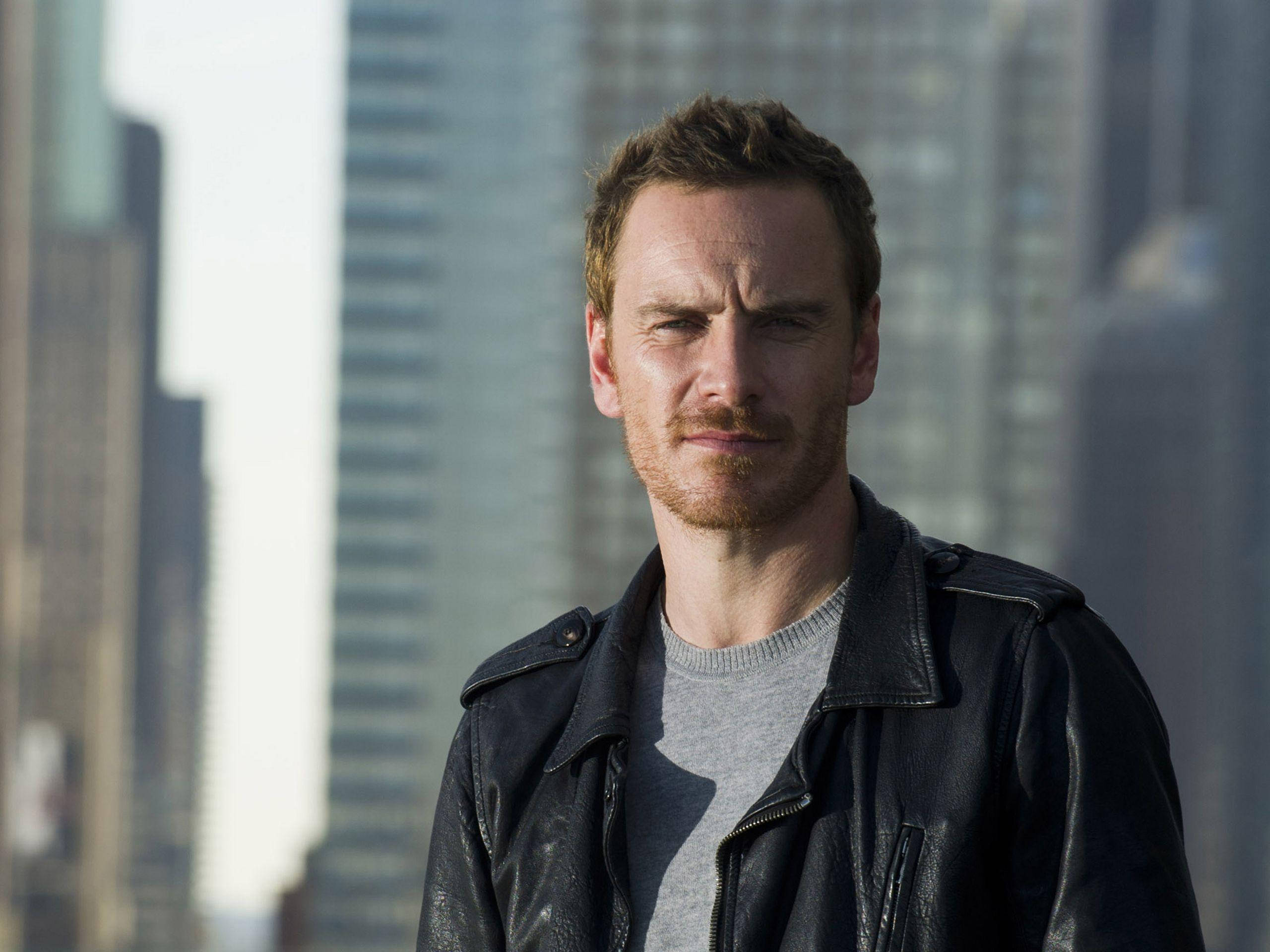 Michael Fassbender, black leather jacket, blurred city skyline, 2K Desktop Wallpaper