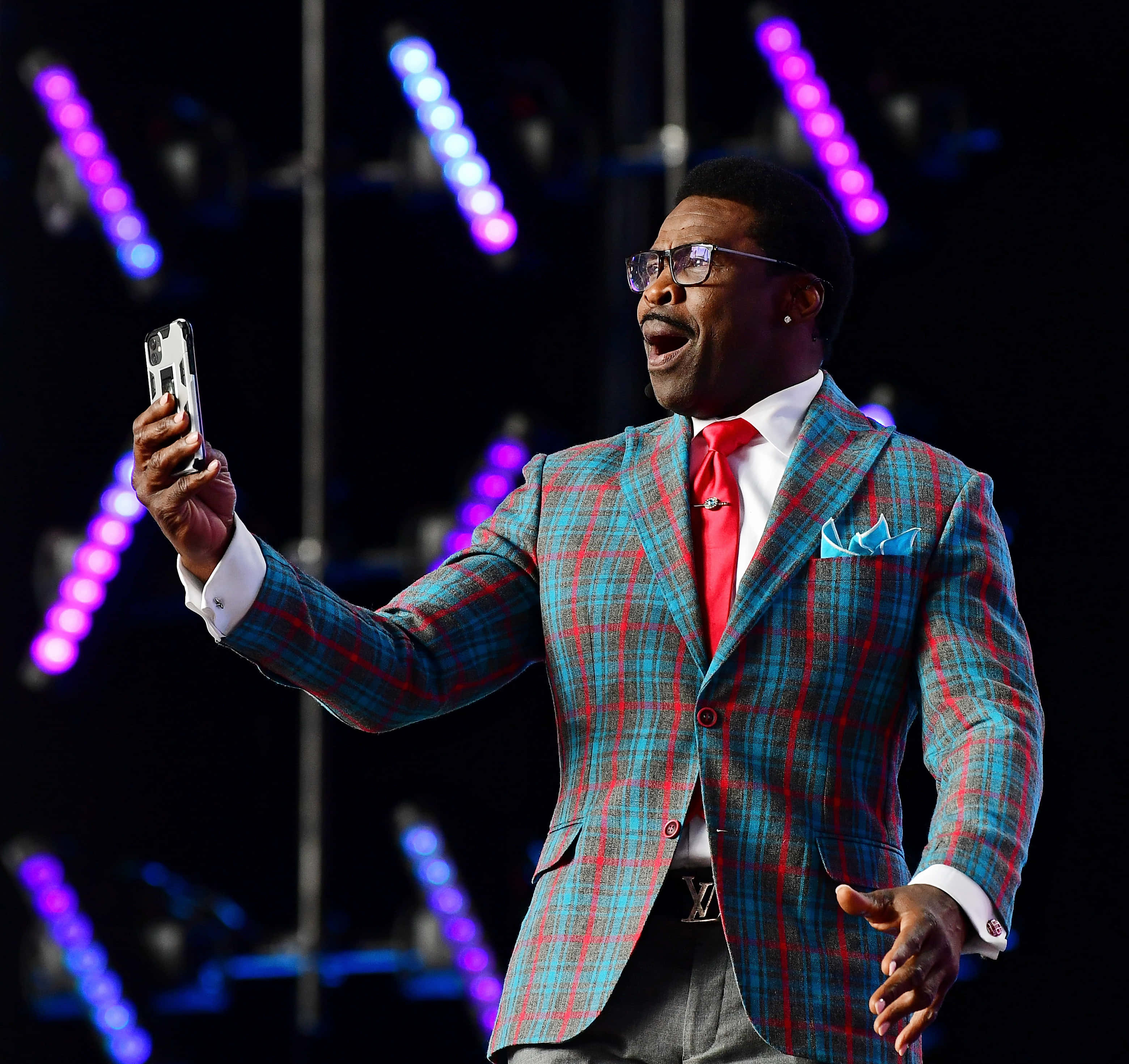 Michael Irvin, vibrant red and teal plaid suit, glowing purple and blue lights, 2K Desktop Wallpaper