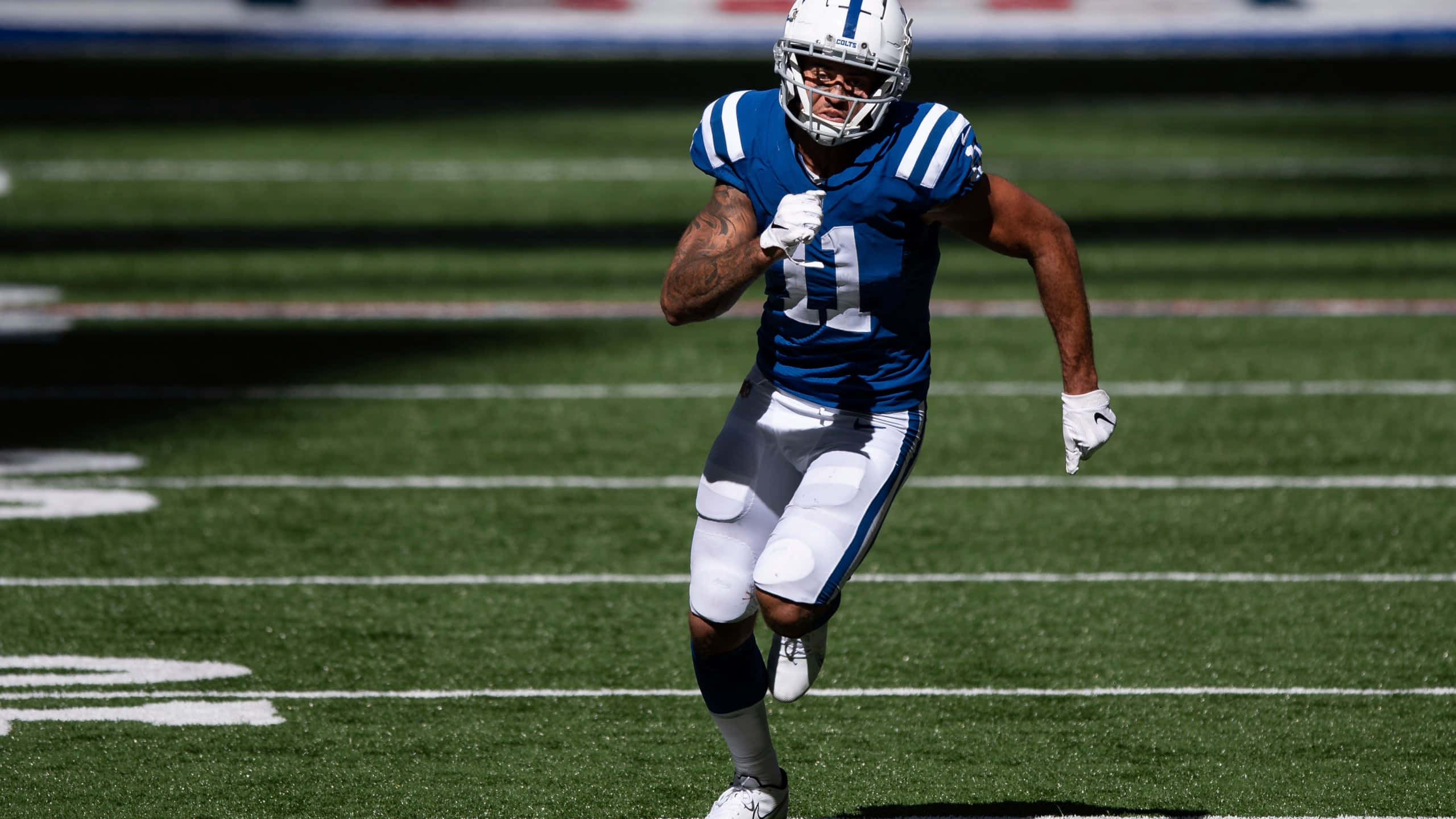 Michael Pittman Jr, blue and white uniform, sunlit green field, 2K Desktop Wallpaper