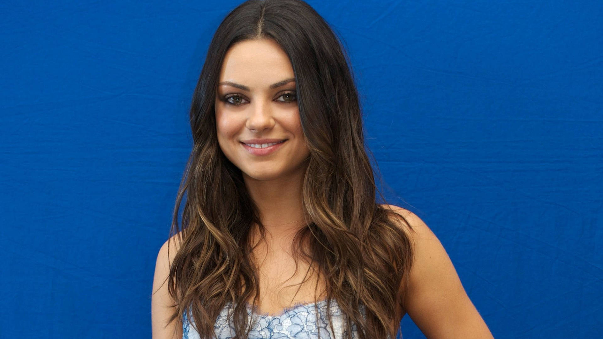 Mila Kunis, long wavy brown hair, solid blue studio backdrop, Full HD Desktop Wallpaper