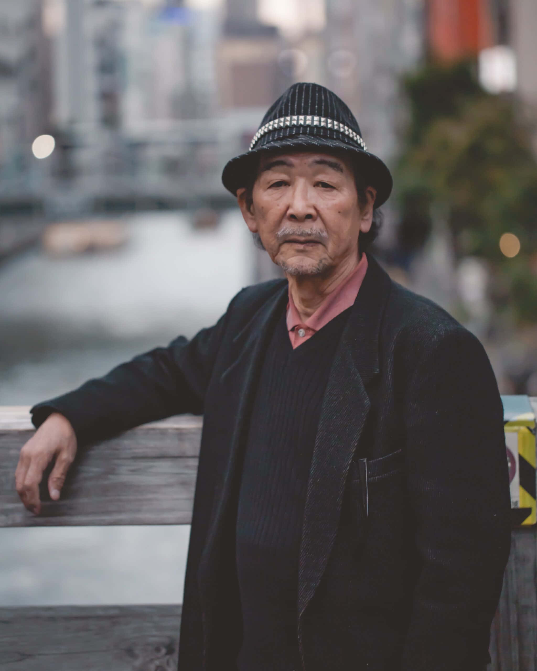 striped fedora, wooden railing, blurred city backdrop, 2K Phone Wallpaper