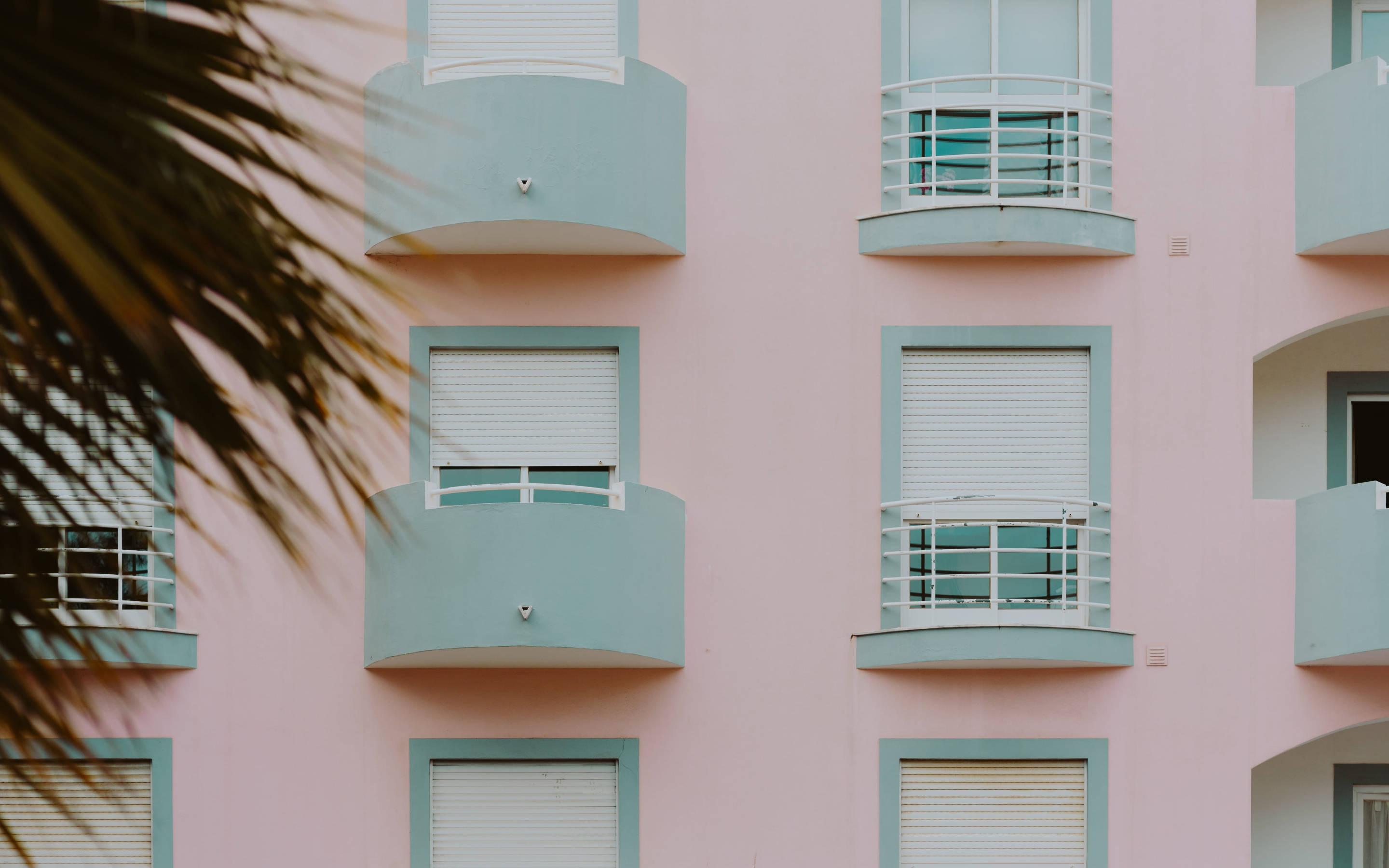 pastel pink apartment building facade, teal balconies, white shutters, 2K Desktop Wallpaper