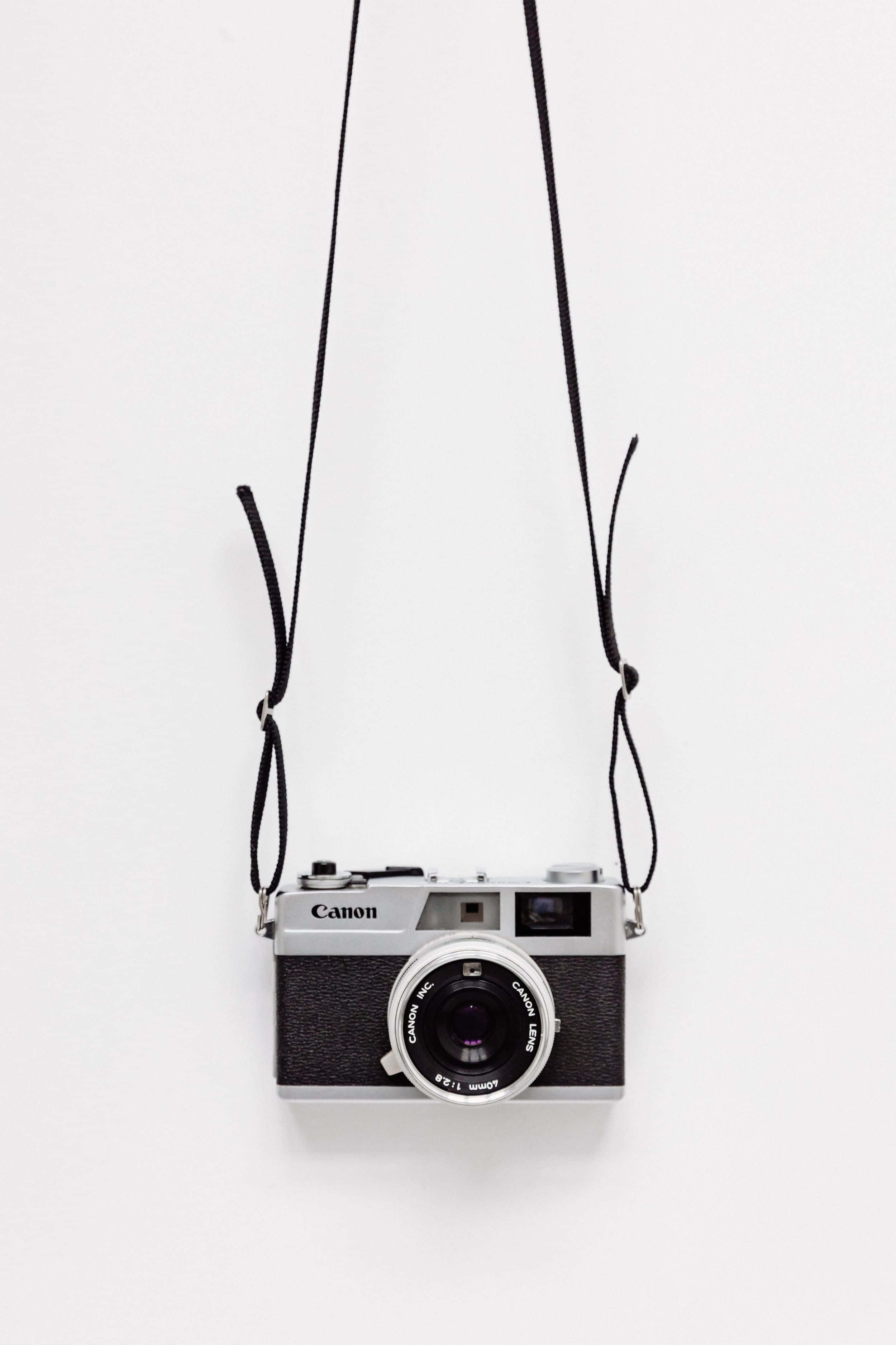 vintage Canon film camera, black strap, stark white background, 2K Phone Wallpaper