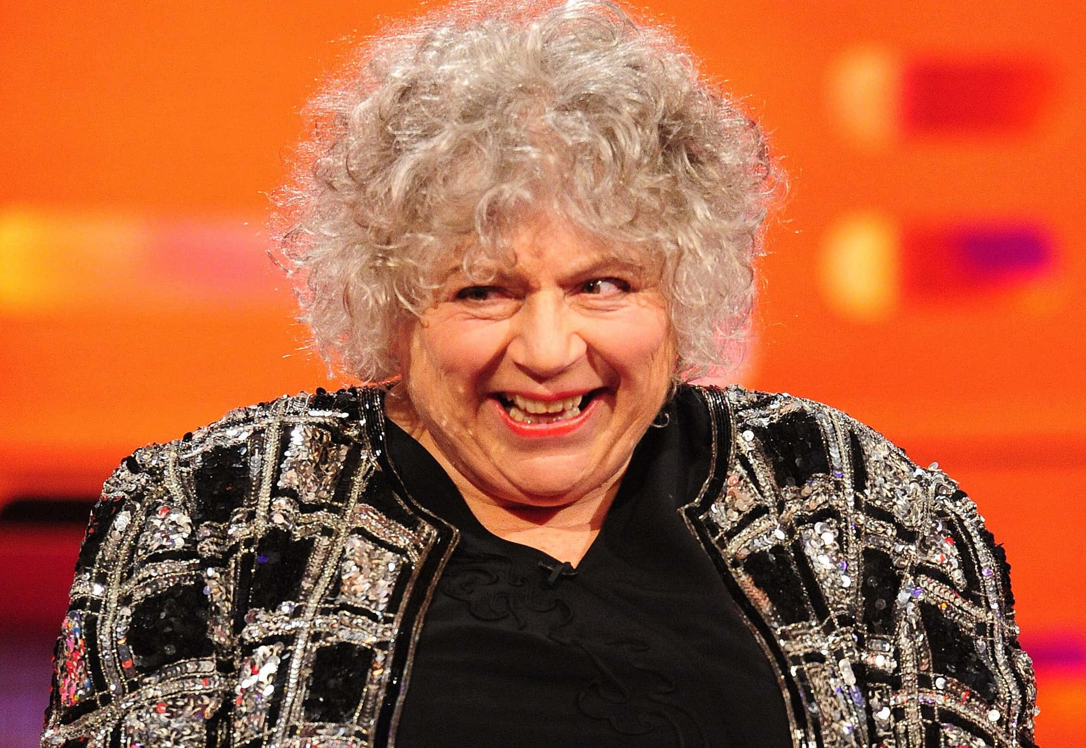 Miriam Margolyes, sparkling black jacket, warm orange background, Full HD Desktop Wallpaper