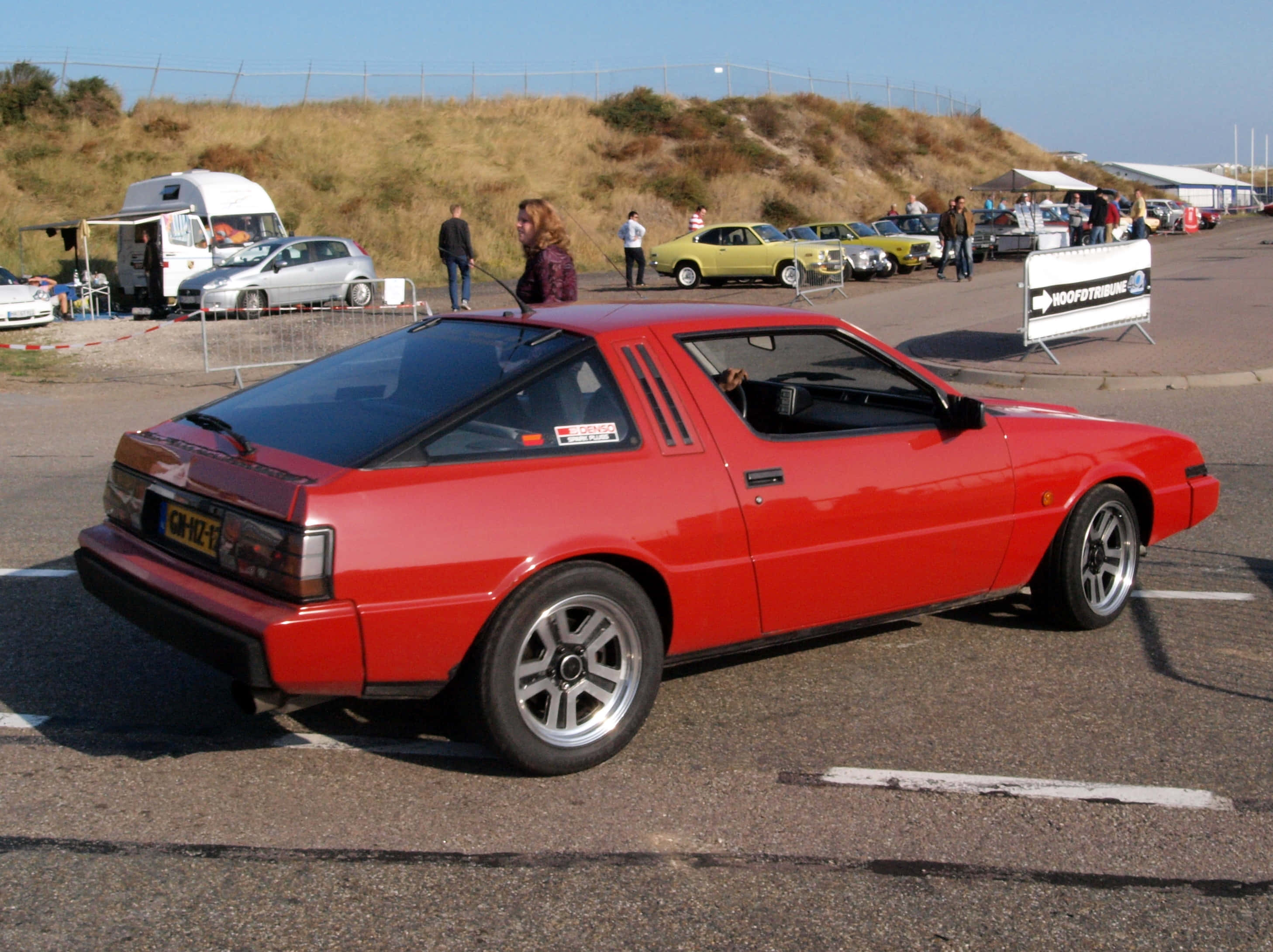 Mitsubishi Starion, vibrant red, sunny outdoor car show, 2K Desktop Wallpaper