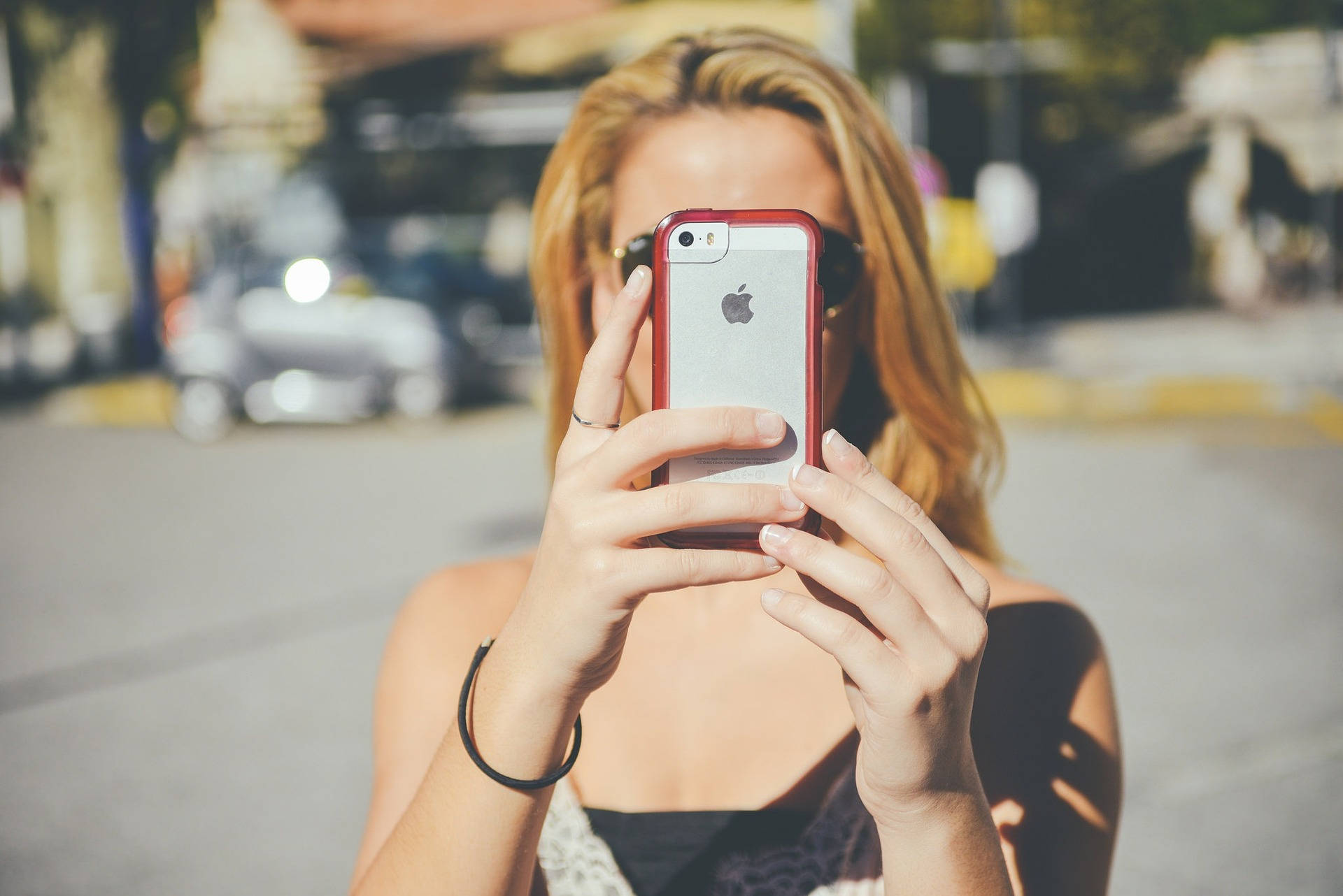 blonde hair, red-cased phone, sunlit city street, Full HD Desktop Wallpaper