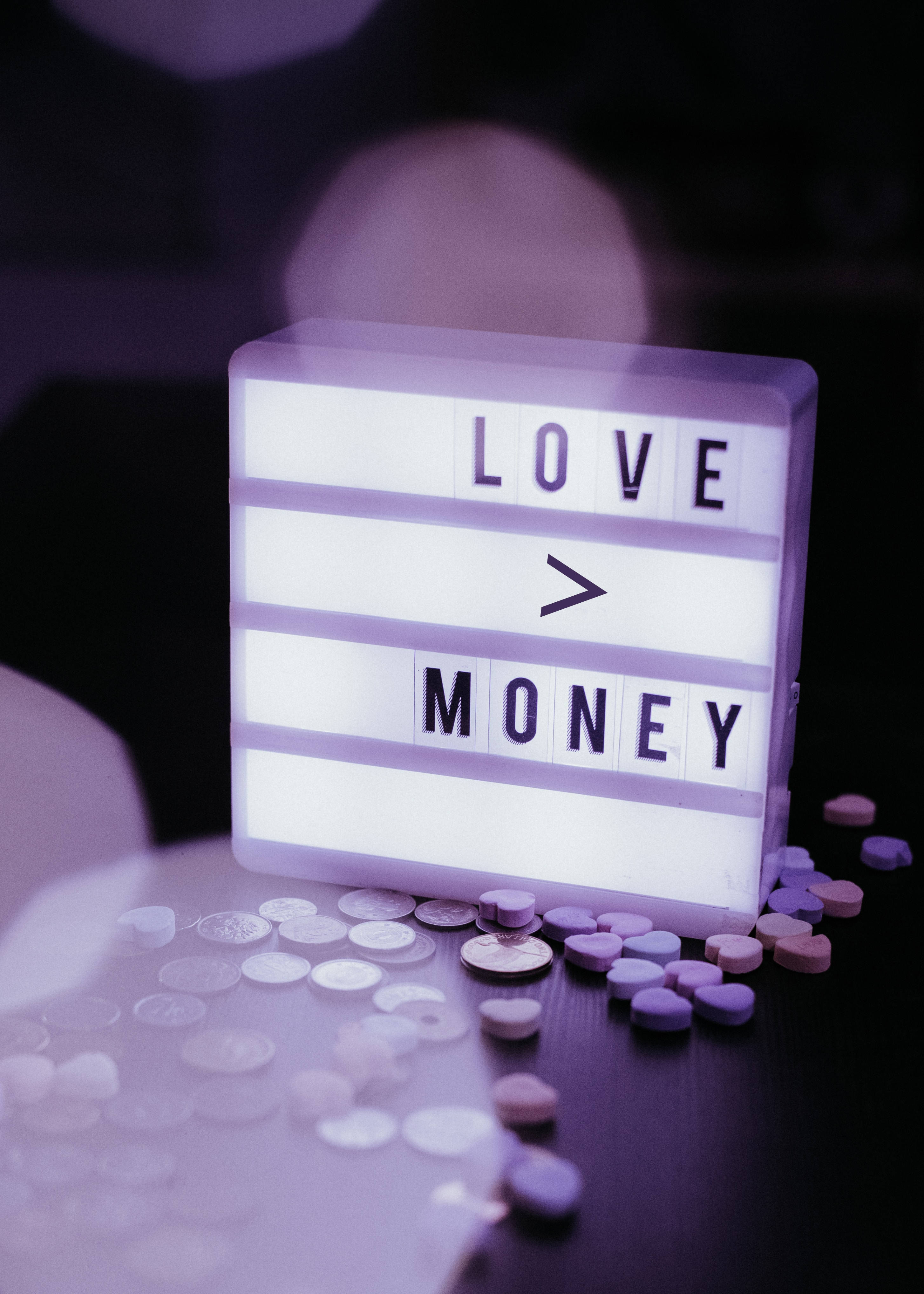 LOVE > MONEY, glowing purple lightbox, scattered coins, 4K Phone Wallpaper