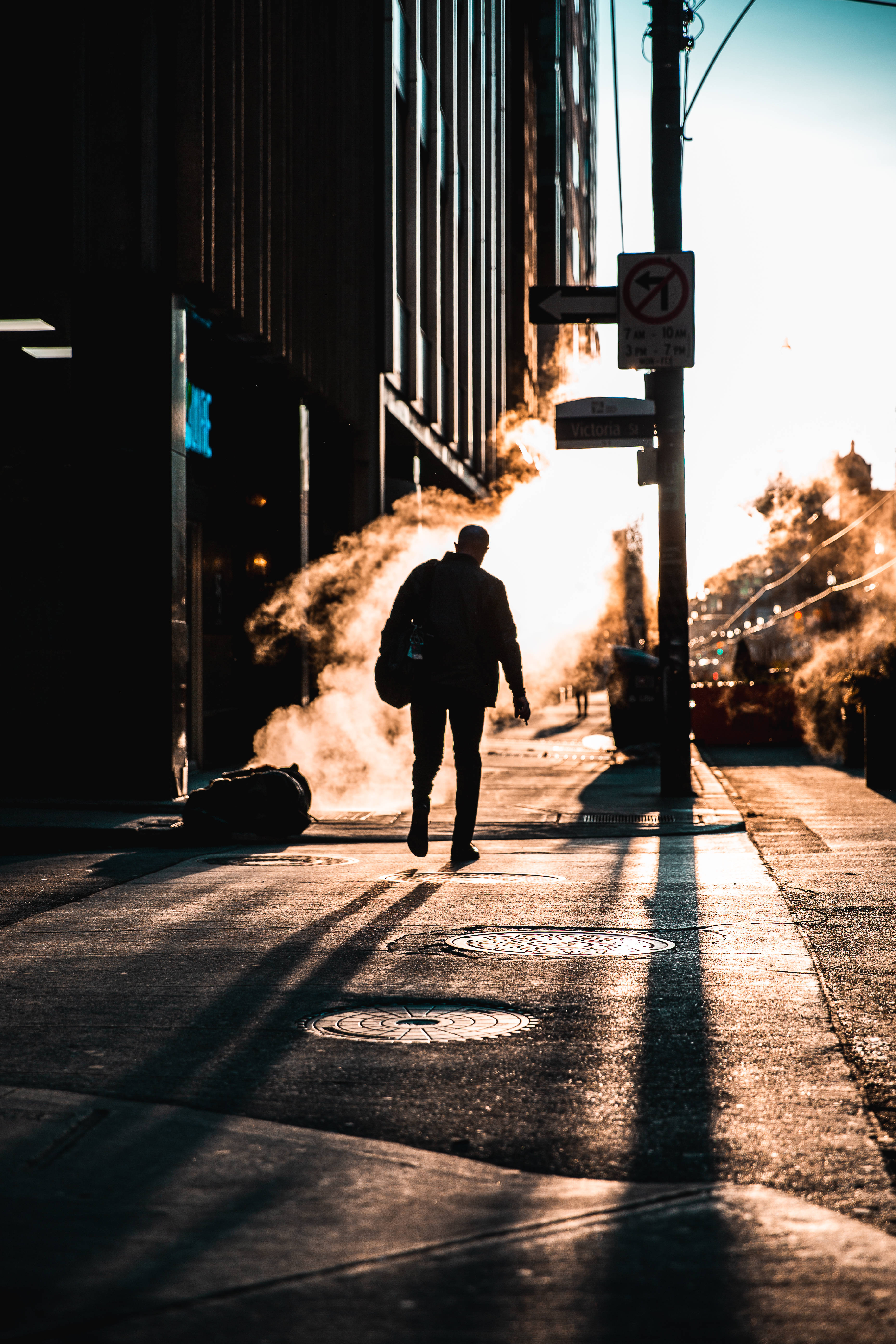 man walking city morning, sunlit urban street, steam from manhole cover, 5K Phone Wallpaper