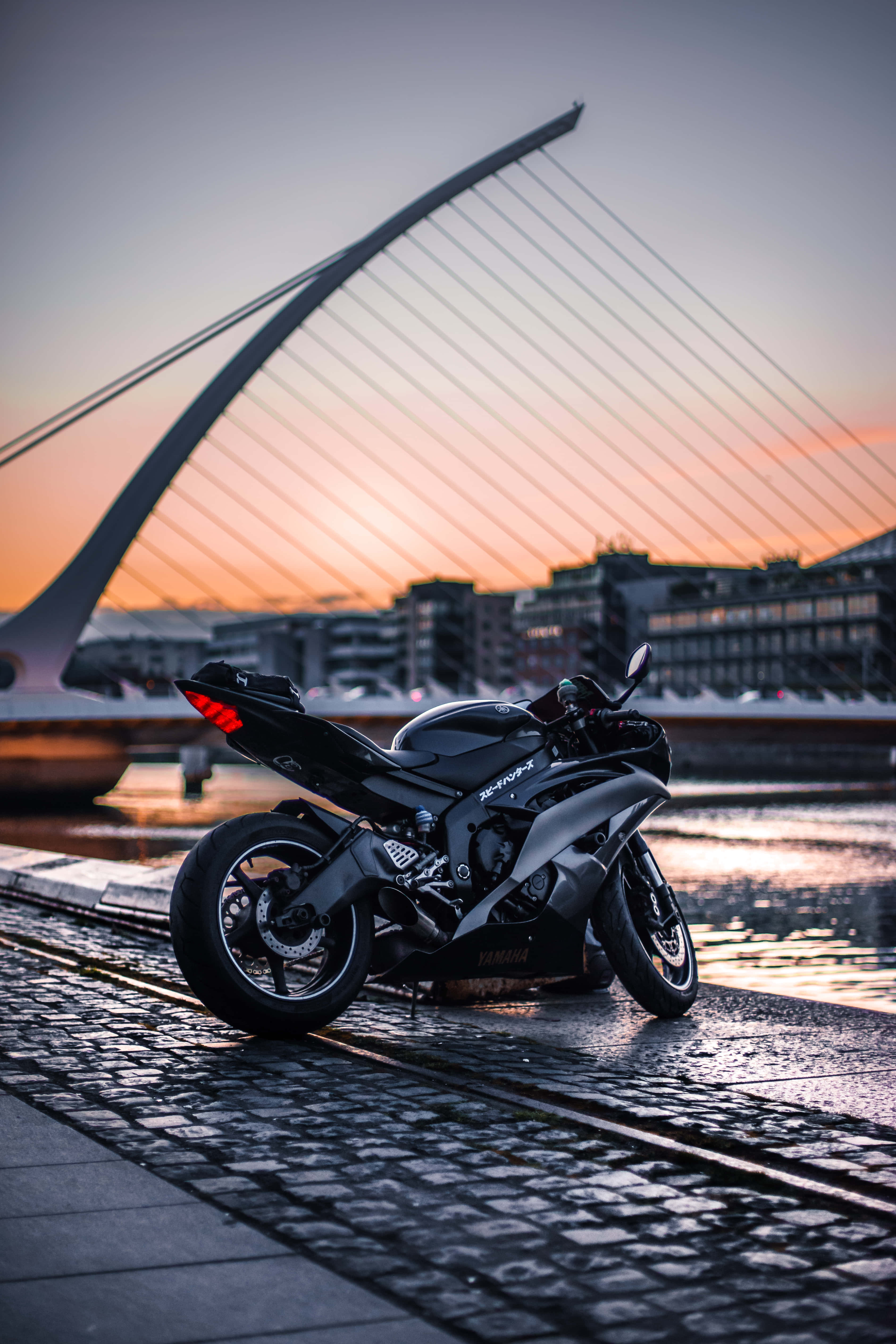 sleek black sport motorcycle, wet cobblestones, sunset, 5K Phone Wallpaper