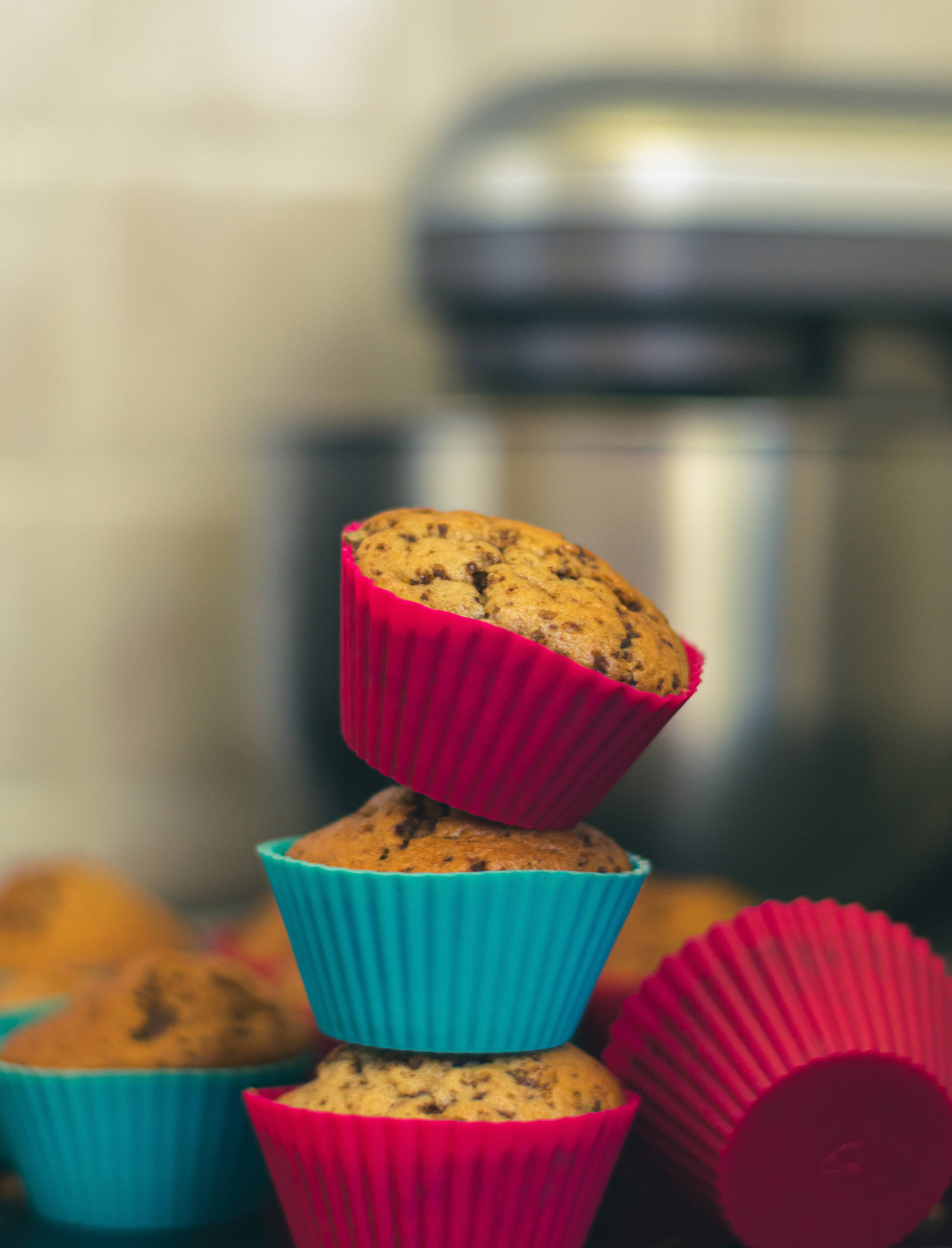 colorful silicone muffin cups, warm chocolate chip muffins, cozy kitchen setting, 2K Phone Wallpaper