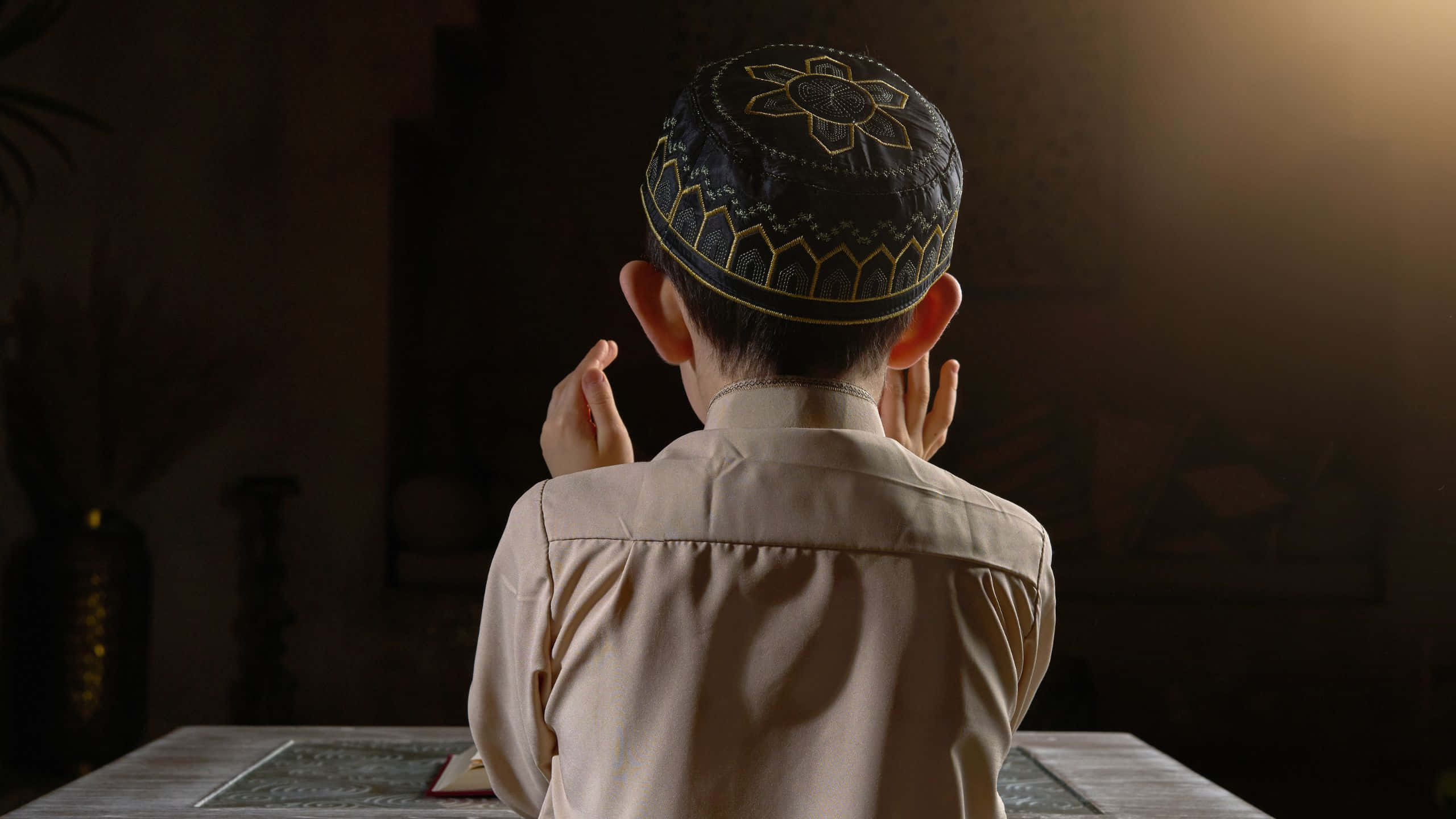 praying muslim boy, patterned cap, dimly lit room, 2K Desktop Wallpaper