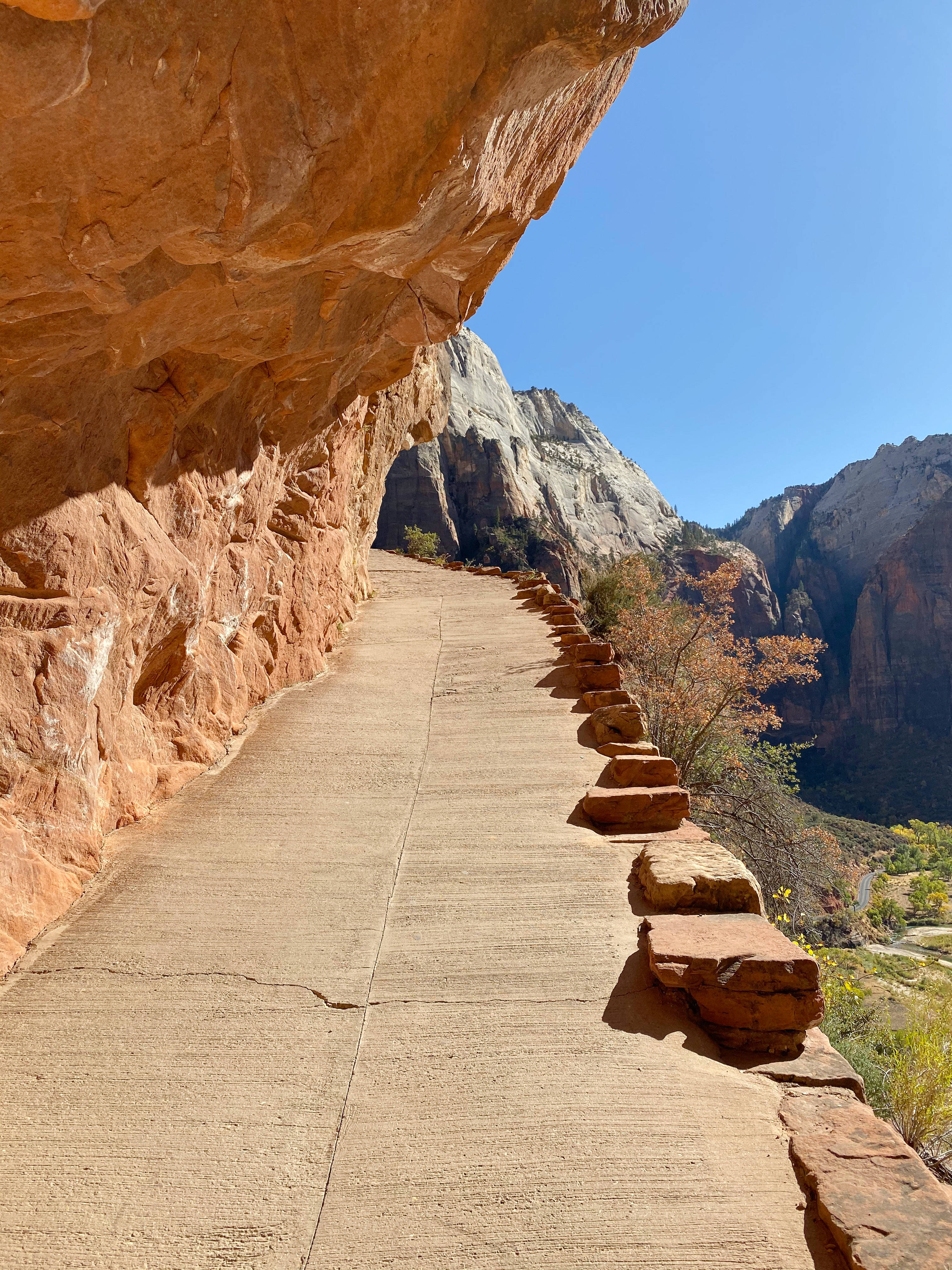 mountainside road, sunlit concrete path, massive orange sandstone overhang, 4K Phone Wallpaper