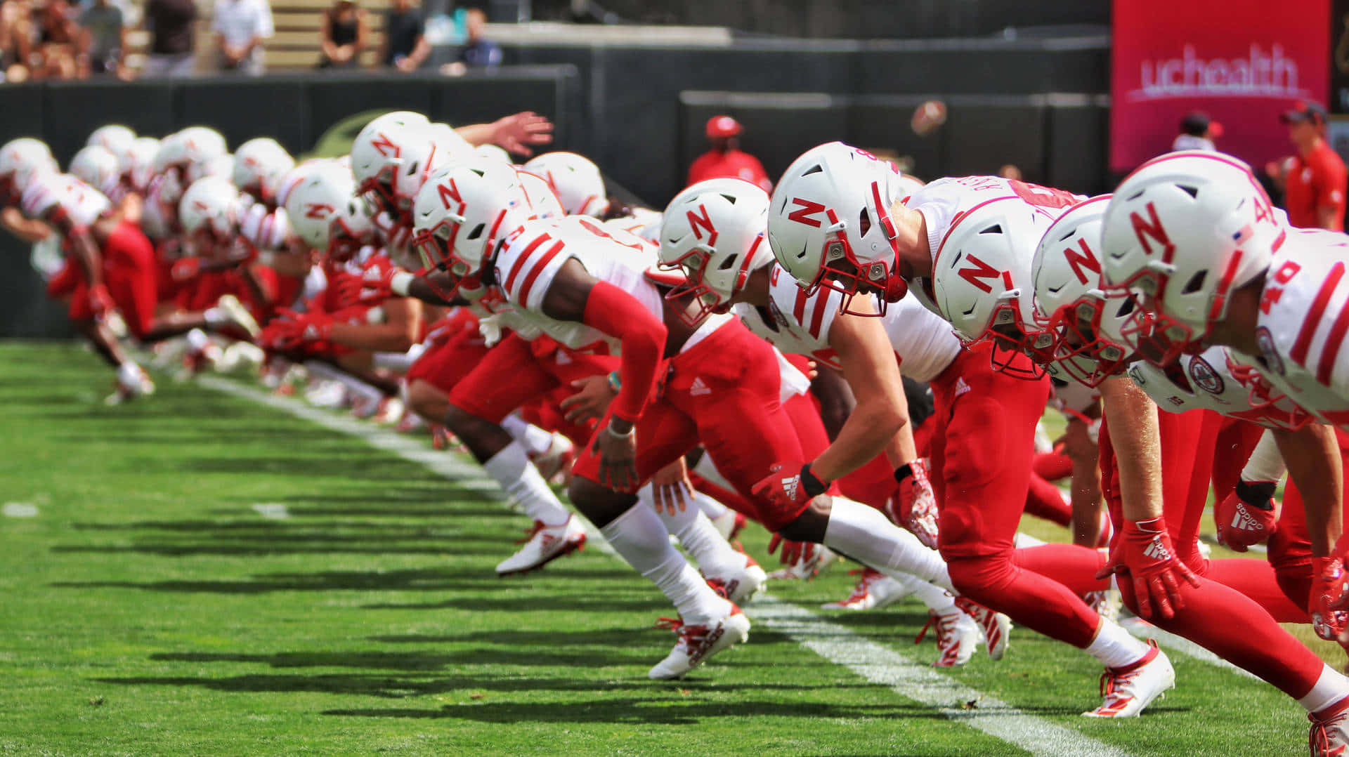 Nebraska Huskers, red and white uniforms, sunlit green field, Full HD Desktop Wallpaper