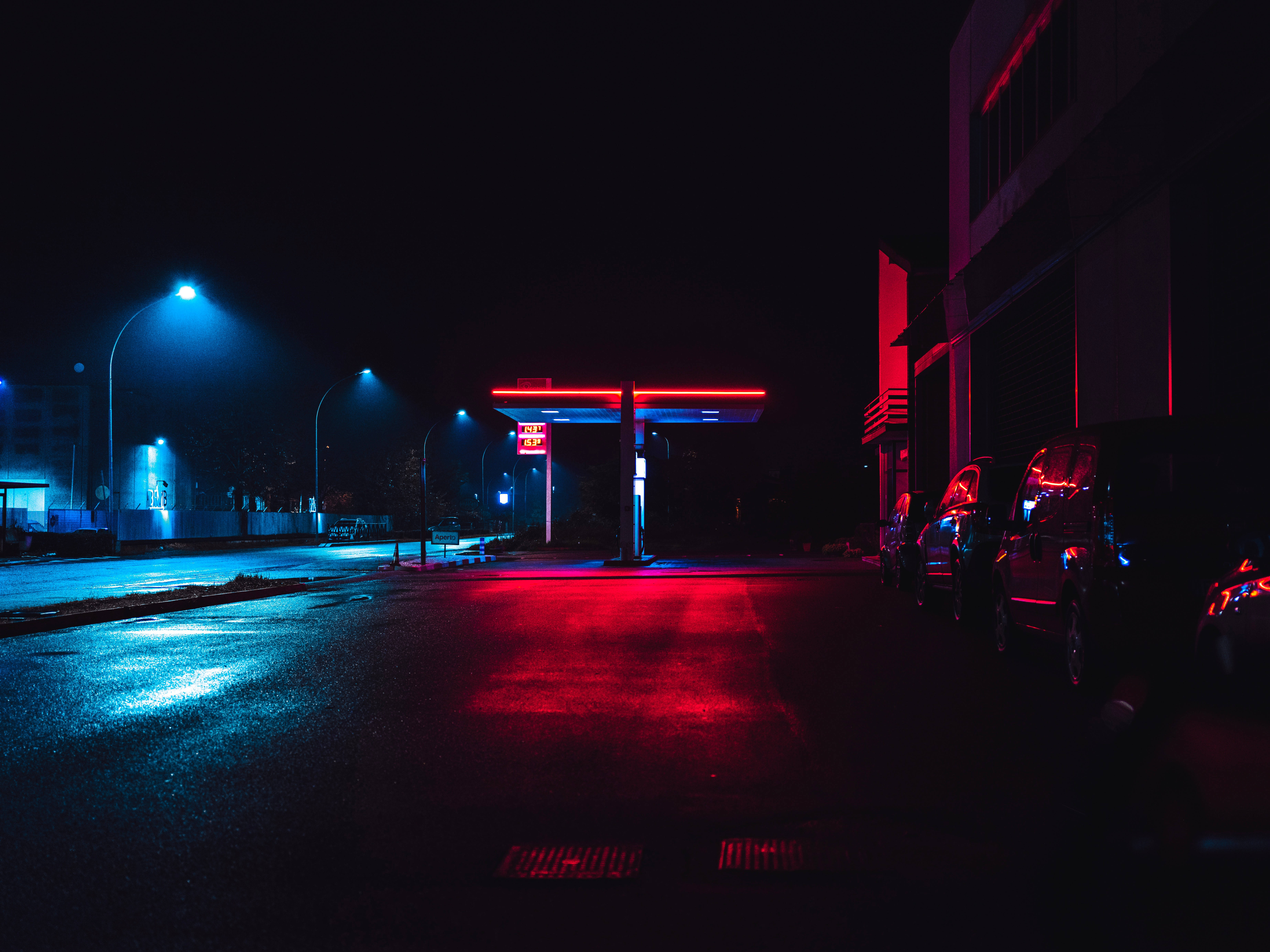 neon-lit gas station, red and blue lights, wet pavement, 5K Desktop Wallpaper