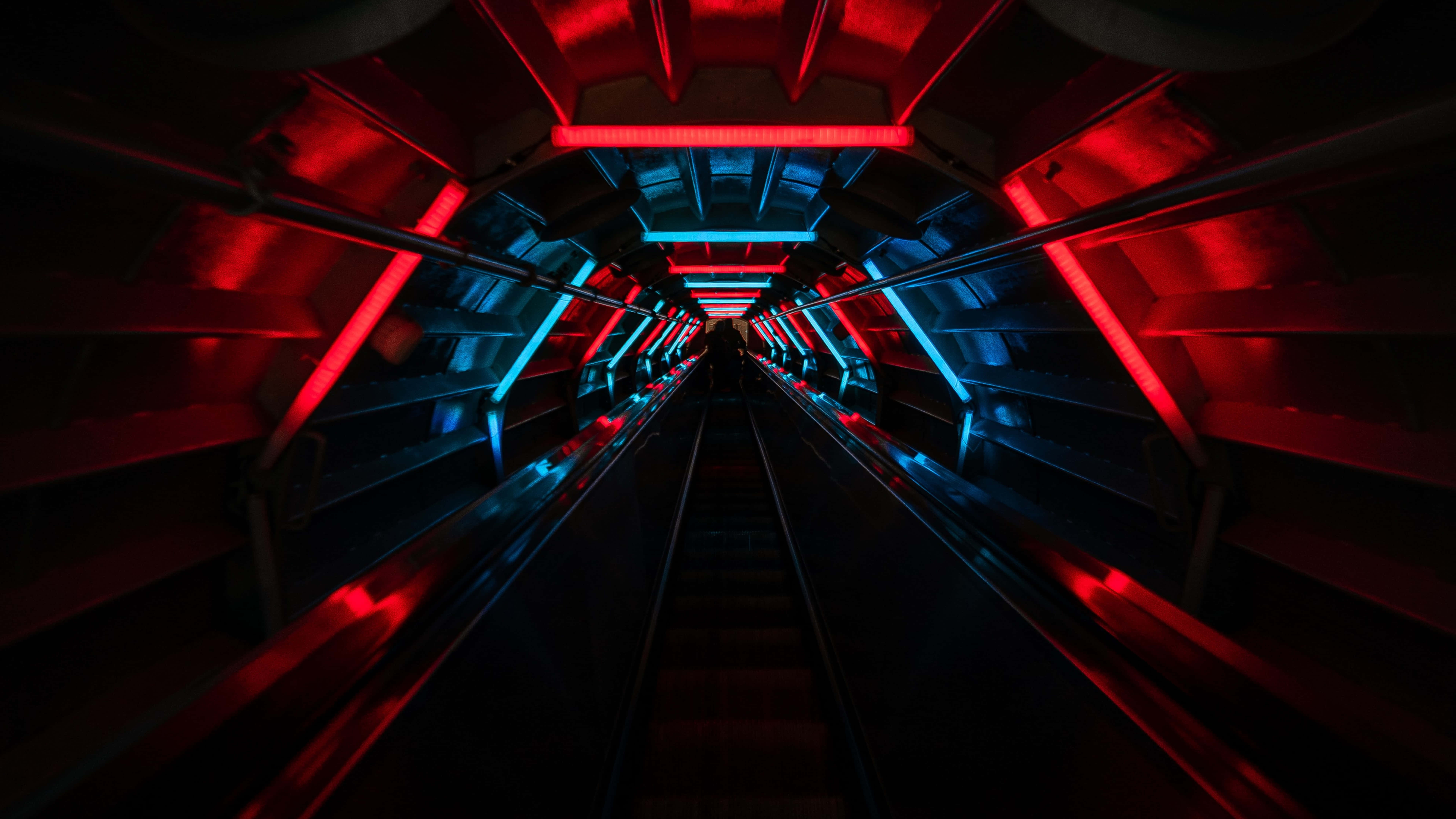 futuristic escalator tunnel, vibrant red and blue neon lights, receding into darkness, 8K Desktop Wallpaper