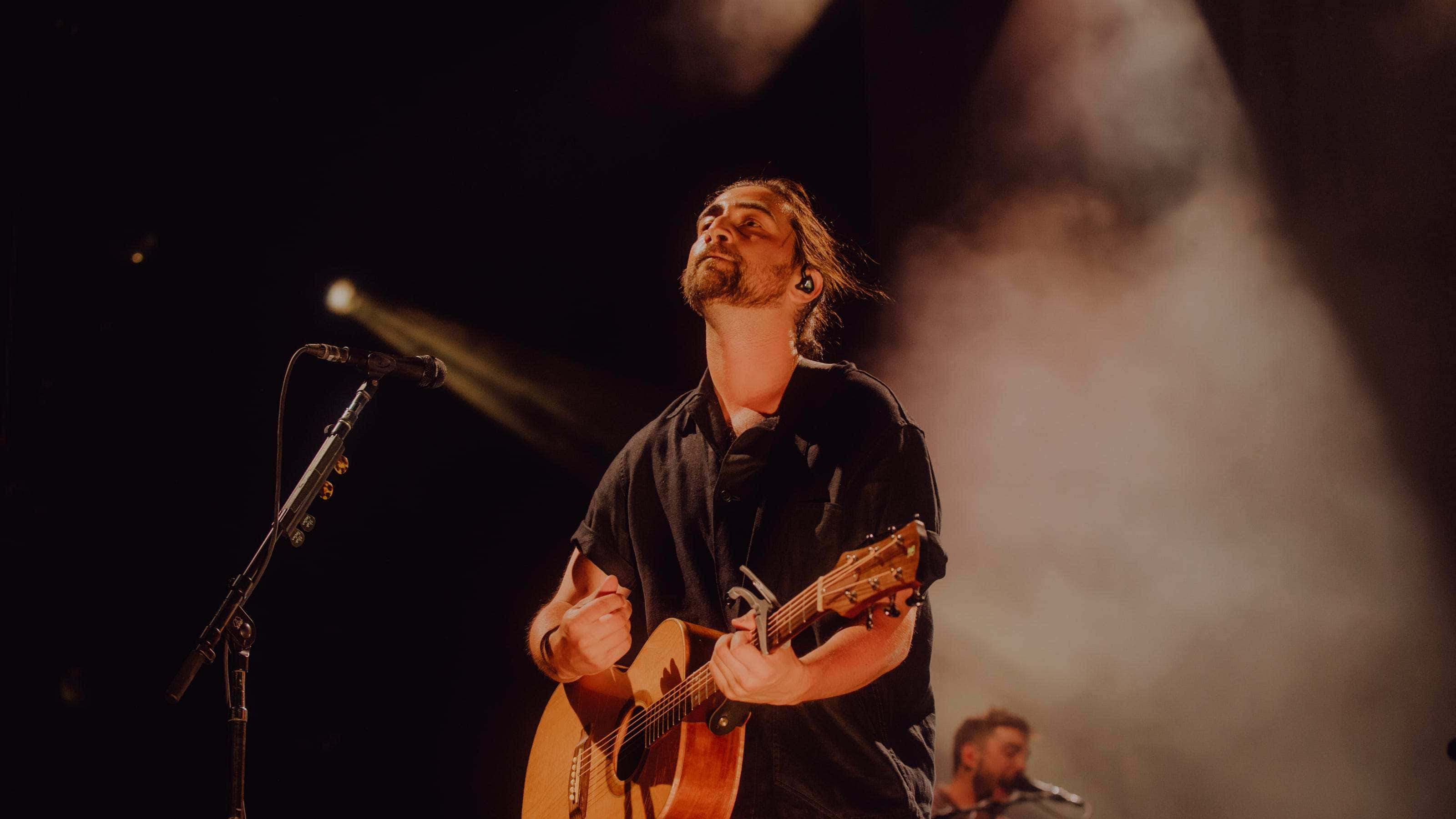 Noah Kahan, acoustic guitar, warm stage lights, 2K Desktop Wallpaper