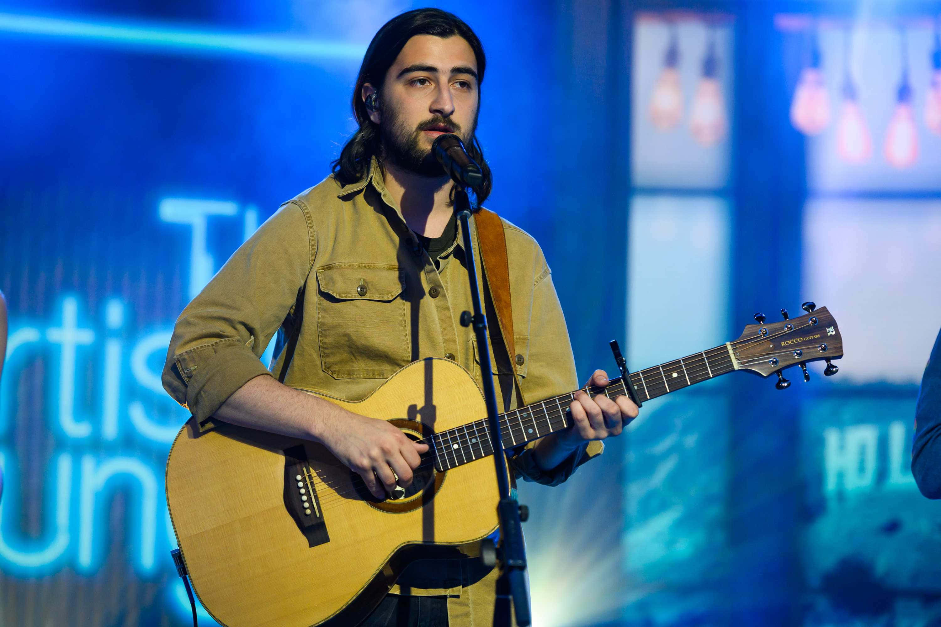 Noah Kahan, acoustic guitar, blue-lit stage, 2K Desktop Wallpaper