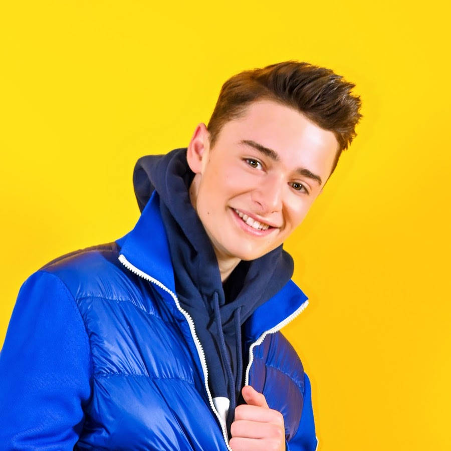 Noah Schnapp, blue puffer jacket, vibrant yellow studio background, SD Desktop Wallpaper