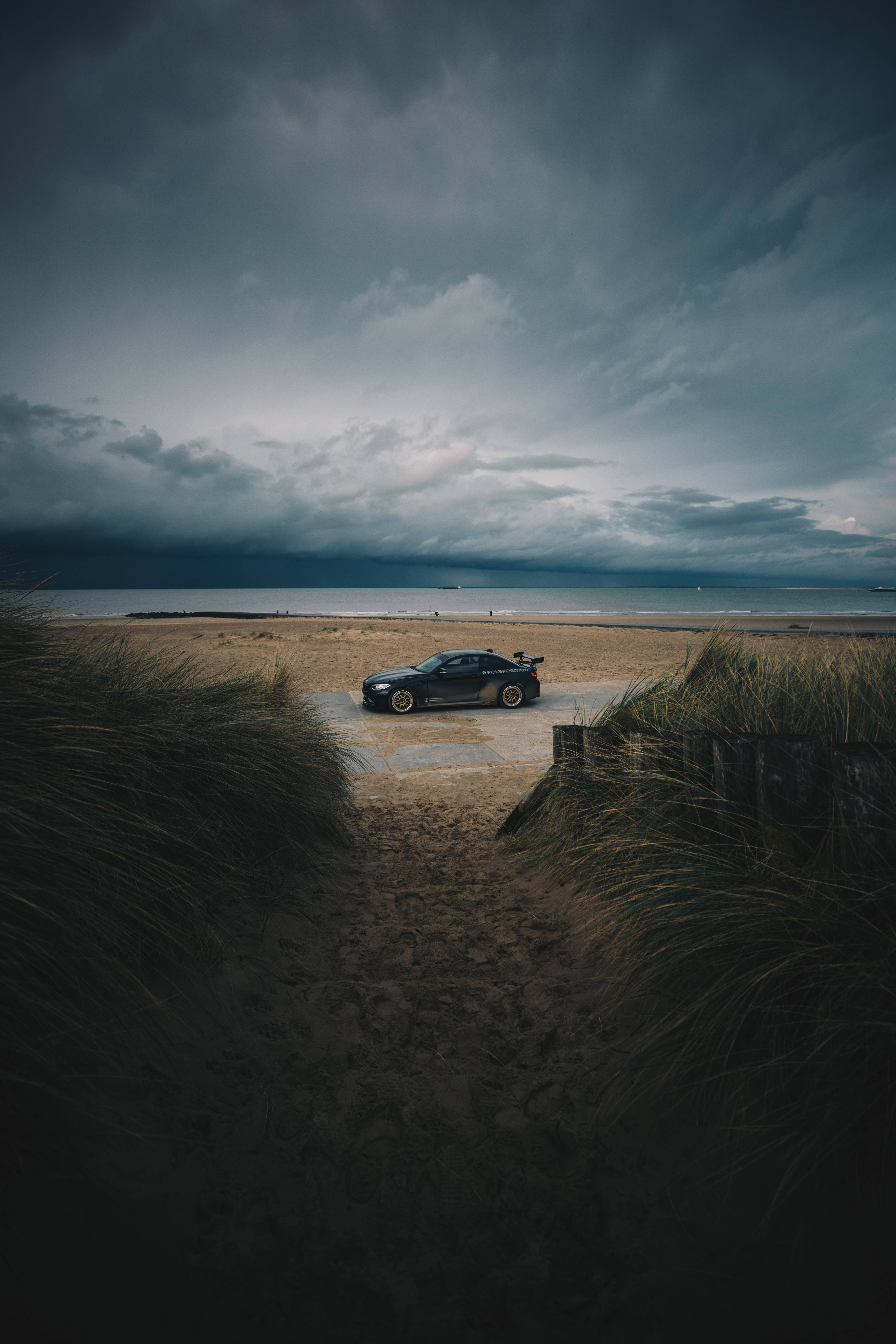 sleek black sports car, concrete pad, grassy dunes, 5K Phone Wallpaper