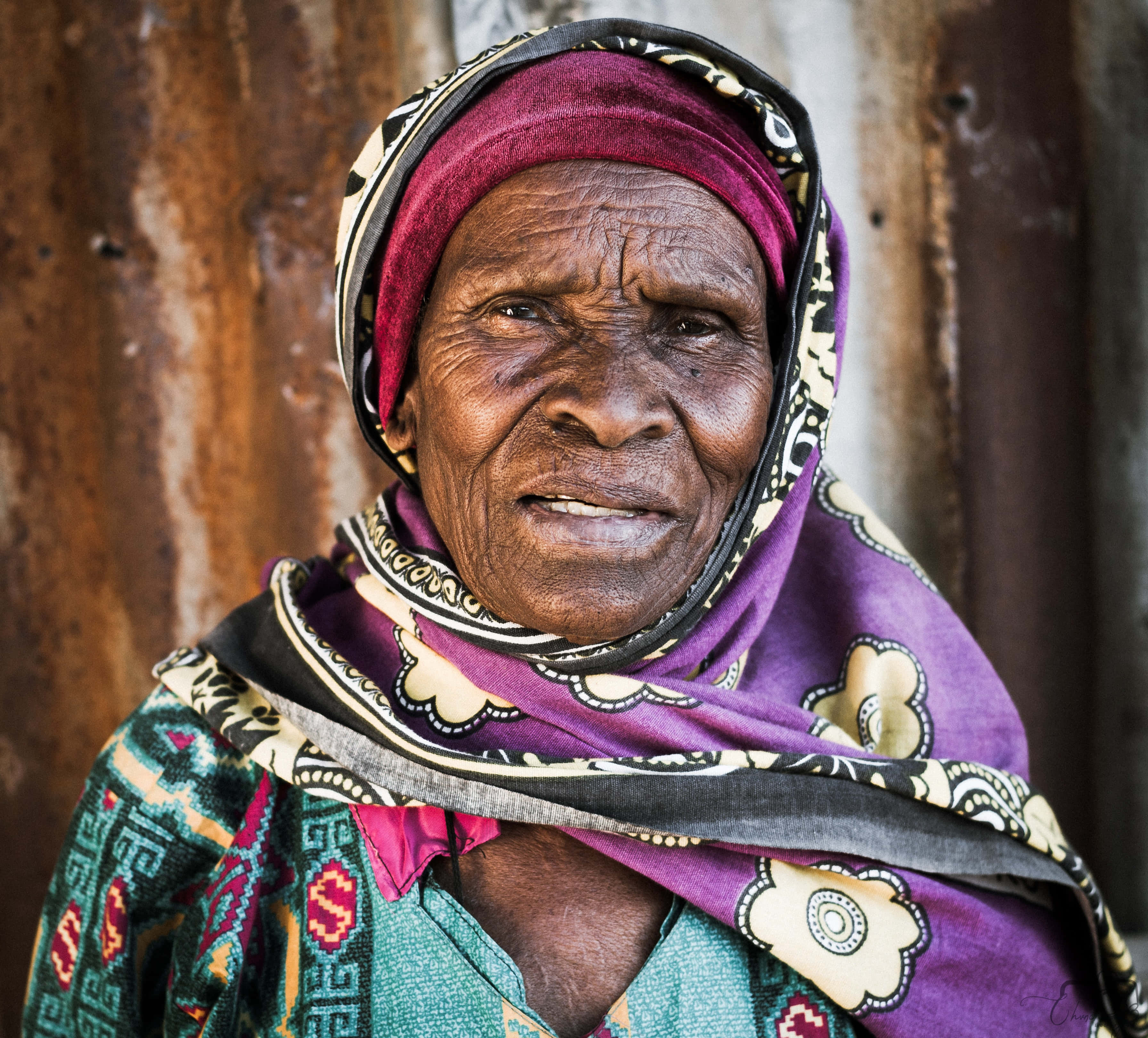 African Old Lady, vibrant patterned headscarf, rusty metal wall, 2K Desktop Wallpaper