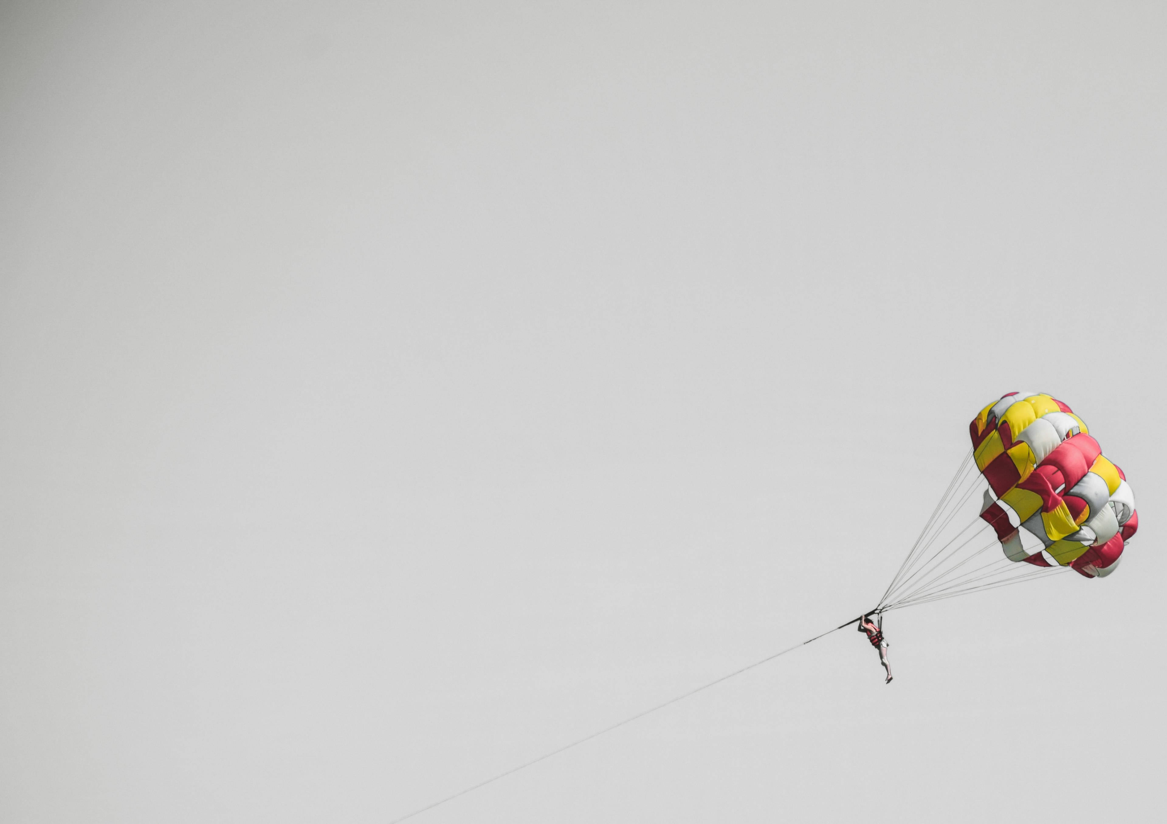 parasailing, vibrant red yellow and white parasail, overcast sky, 4K Desktop Wallpaper