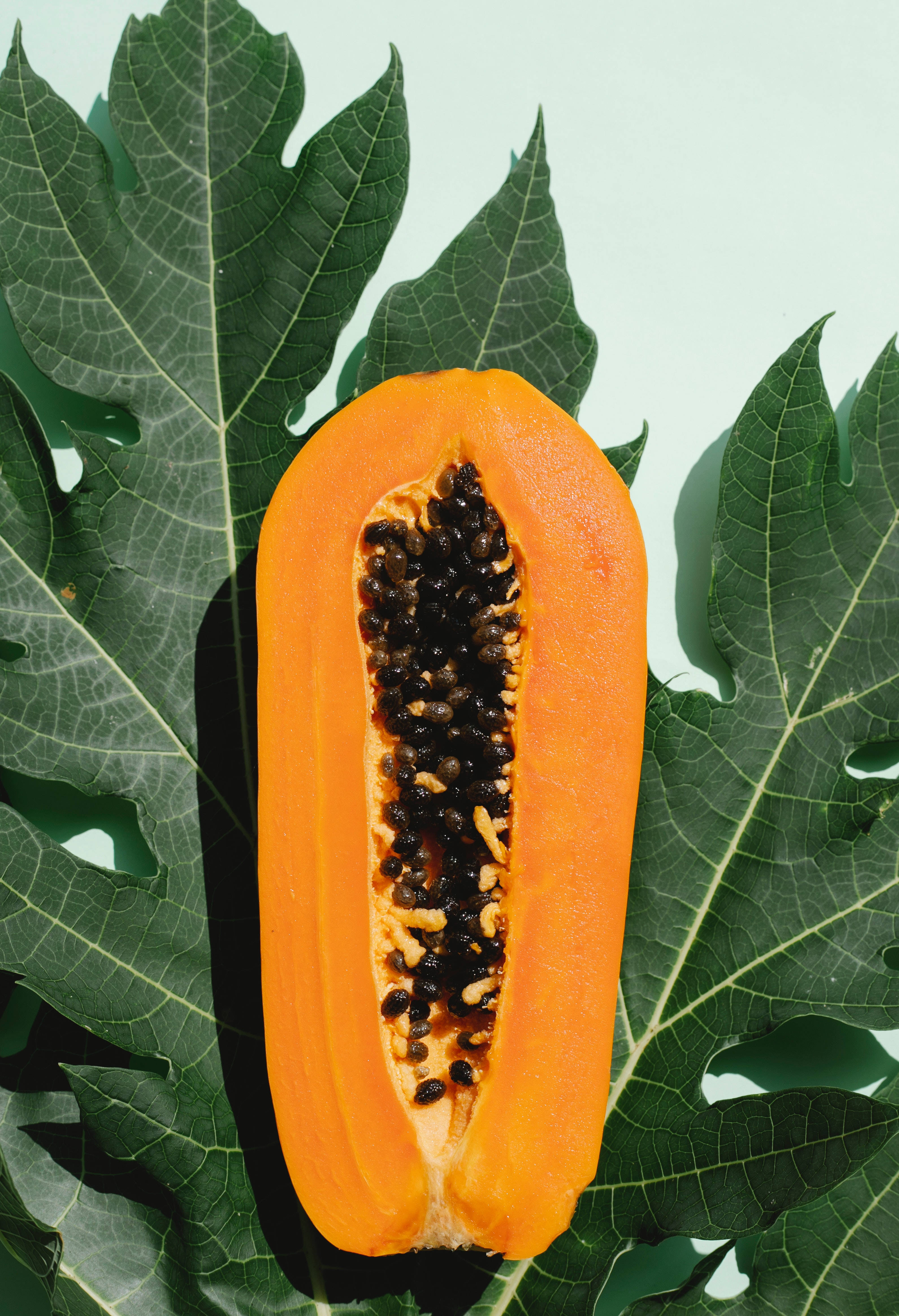 sliced papaya fruit, black seeds, green leaves, 4K Phone Wallpaper