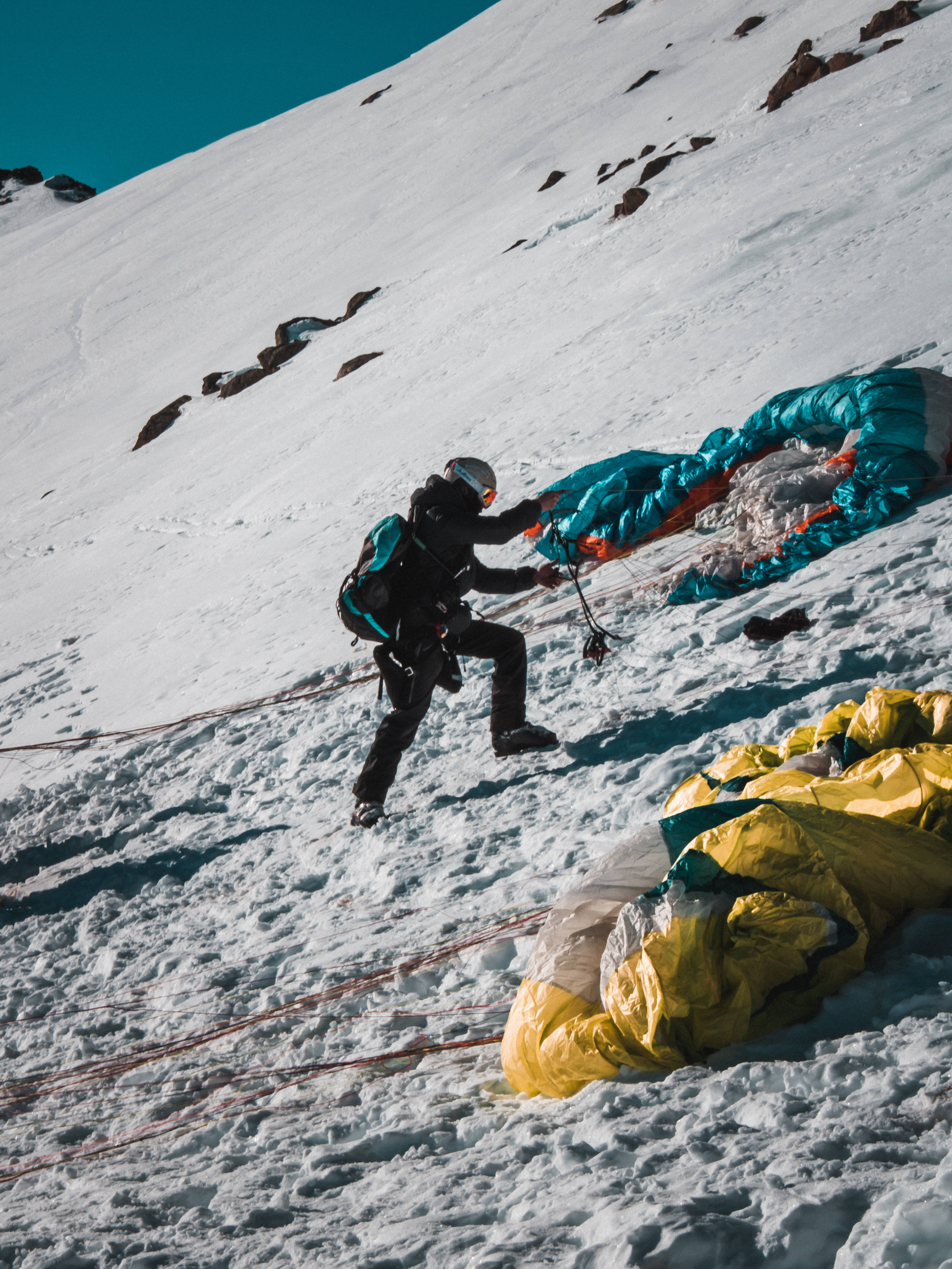 paragliding, snowy mountain slope, vibrant blue and yellow canopies, 5K Phone Wallpaper