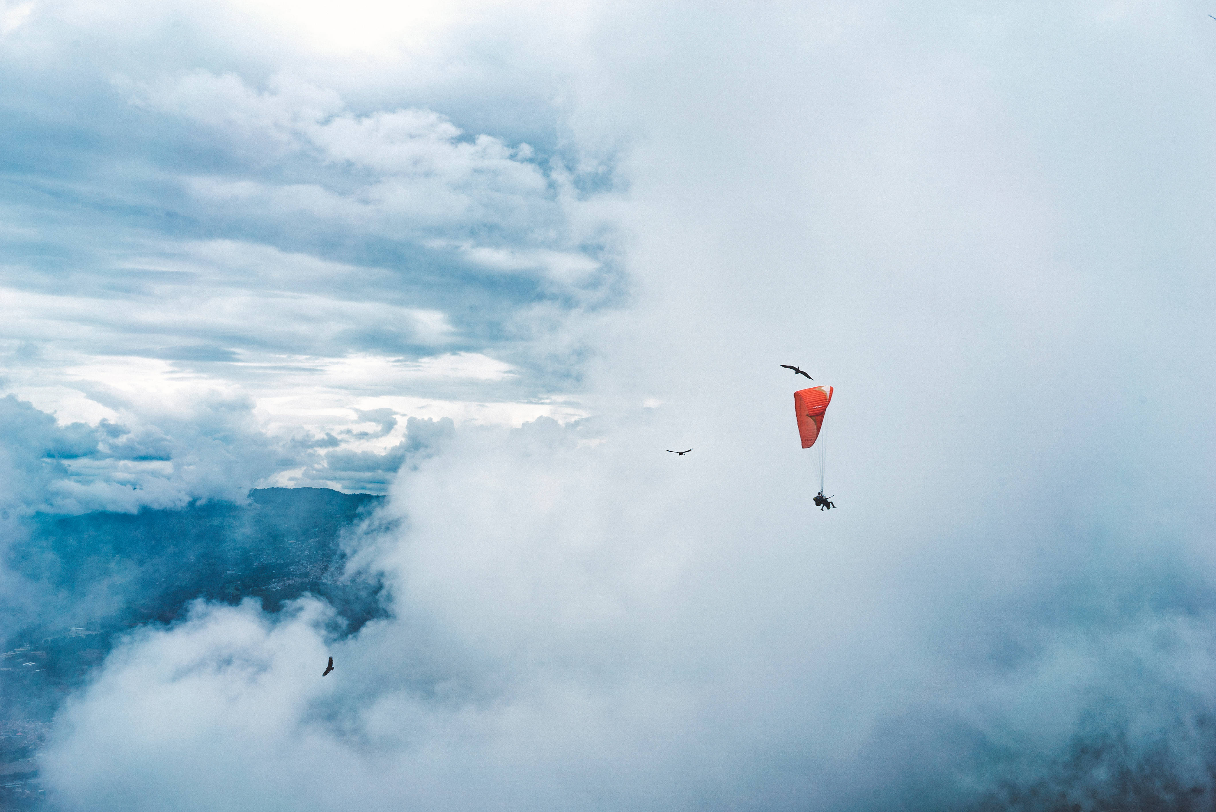 vibrant red paraglider, sea of fluffy white clouds, distant mountains, 4K Desktop Wallpaper
