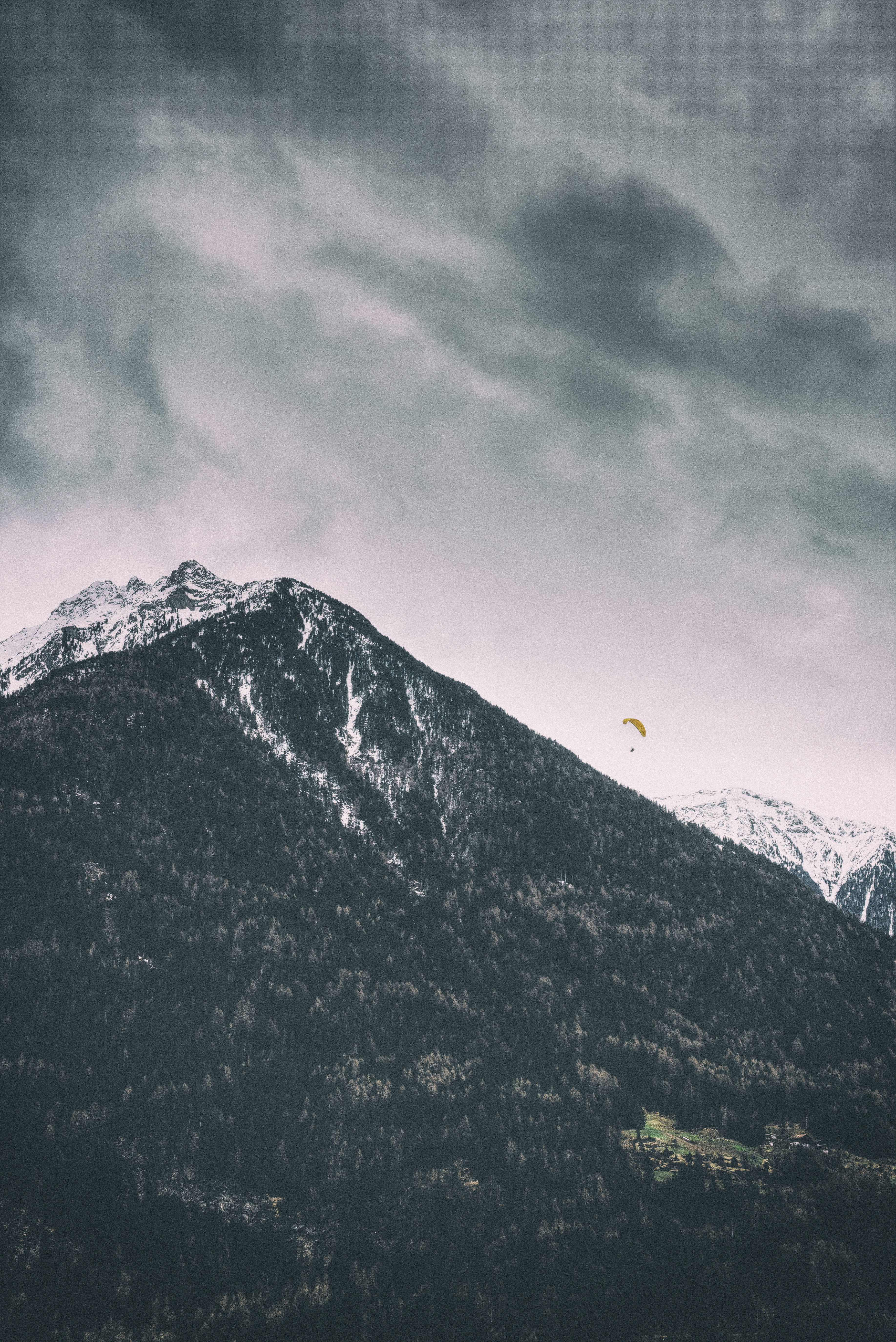 yellow paraglider, snow-dusted mountain peak, moody gray sky, 5K Phone Wallpaper