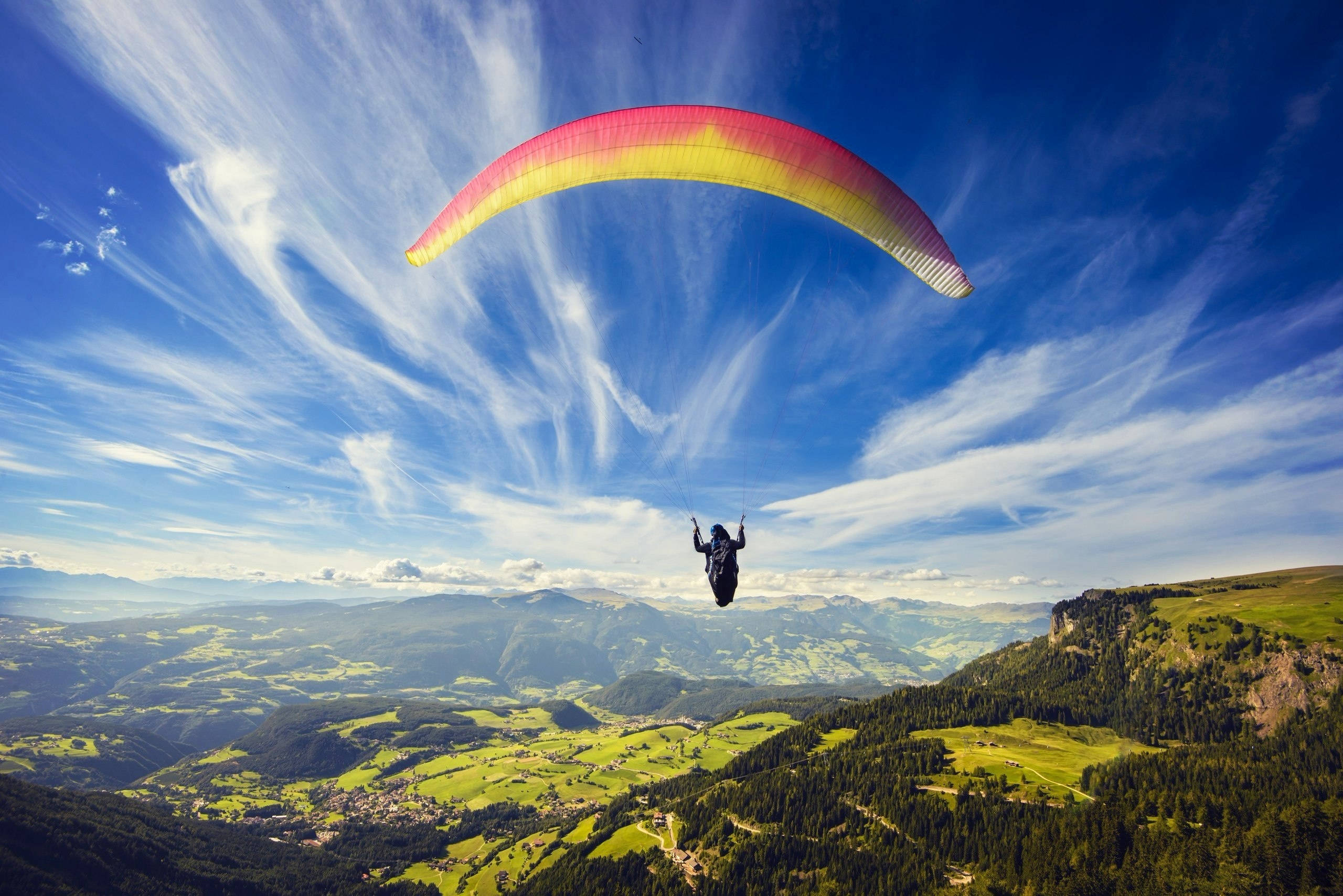 paragliding, vibrant red yellow canopy, sprawling green valley, 2K Desktop Wallpaper