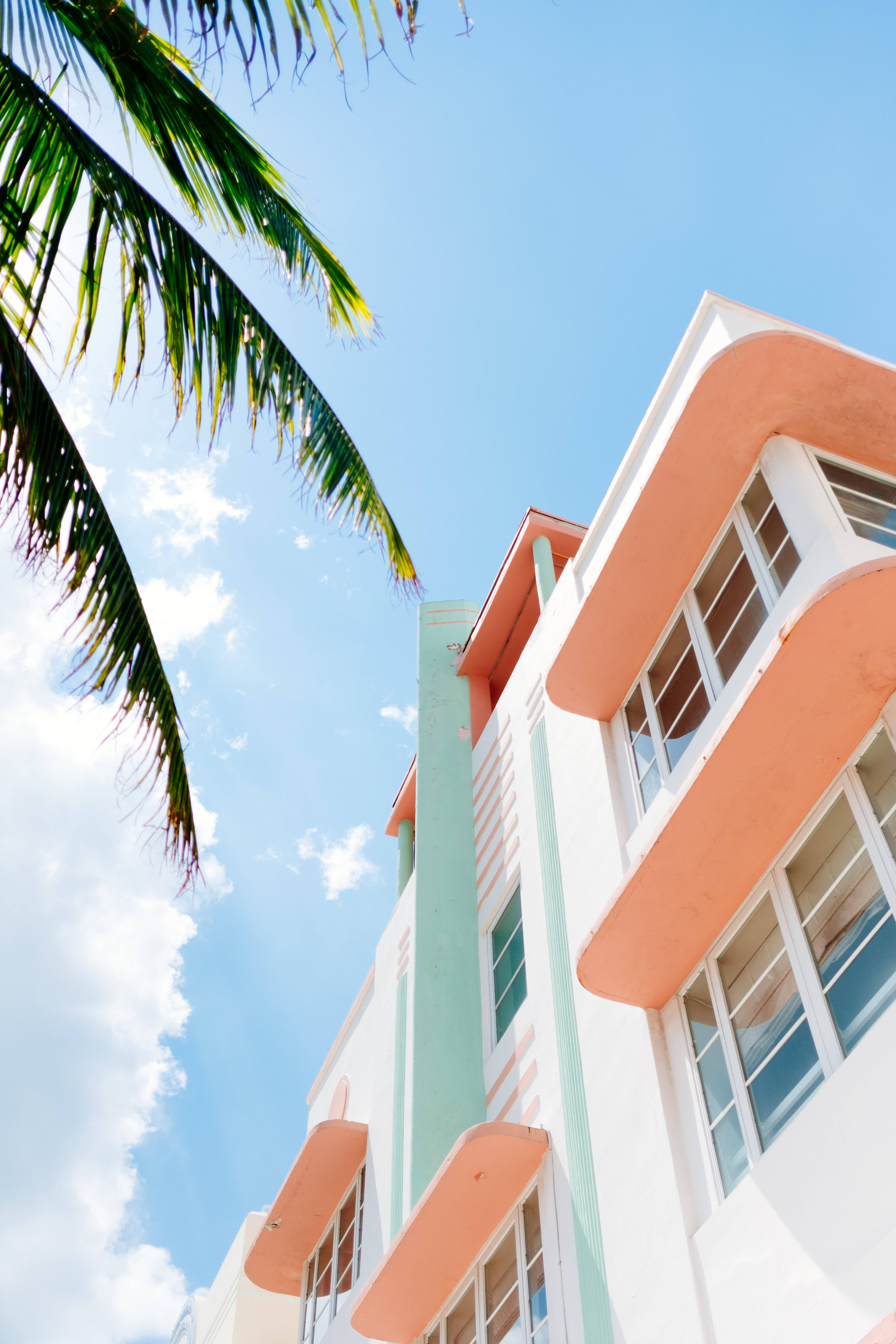 pastel Art Deco building, orange and mint green accents, palm fronds, 5K Phone Wallpaper