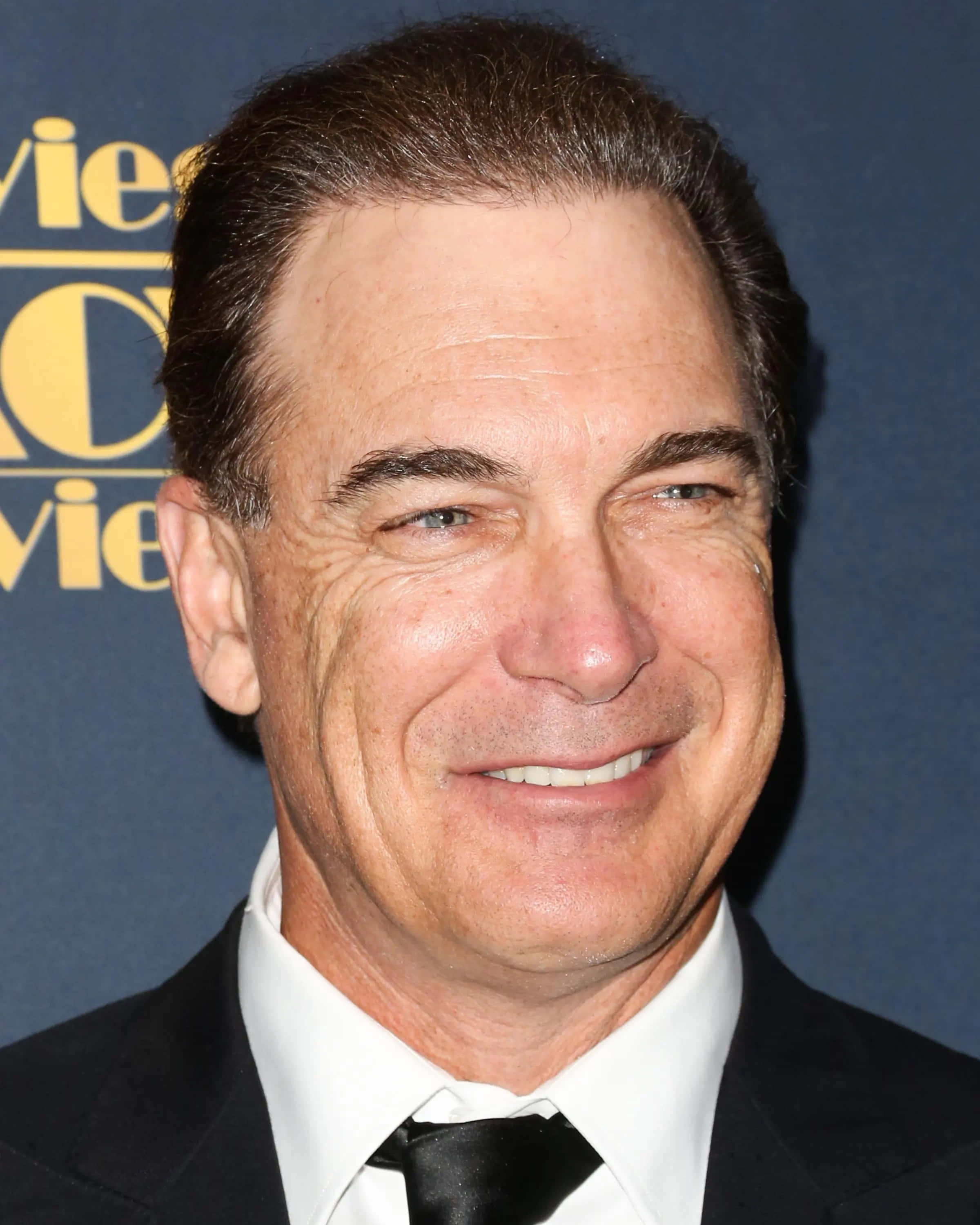 Patrick Warburton, black suit and tie, blue backdrop, 2K Phone Wallpaper