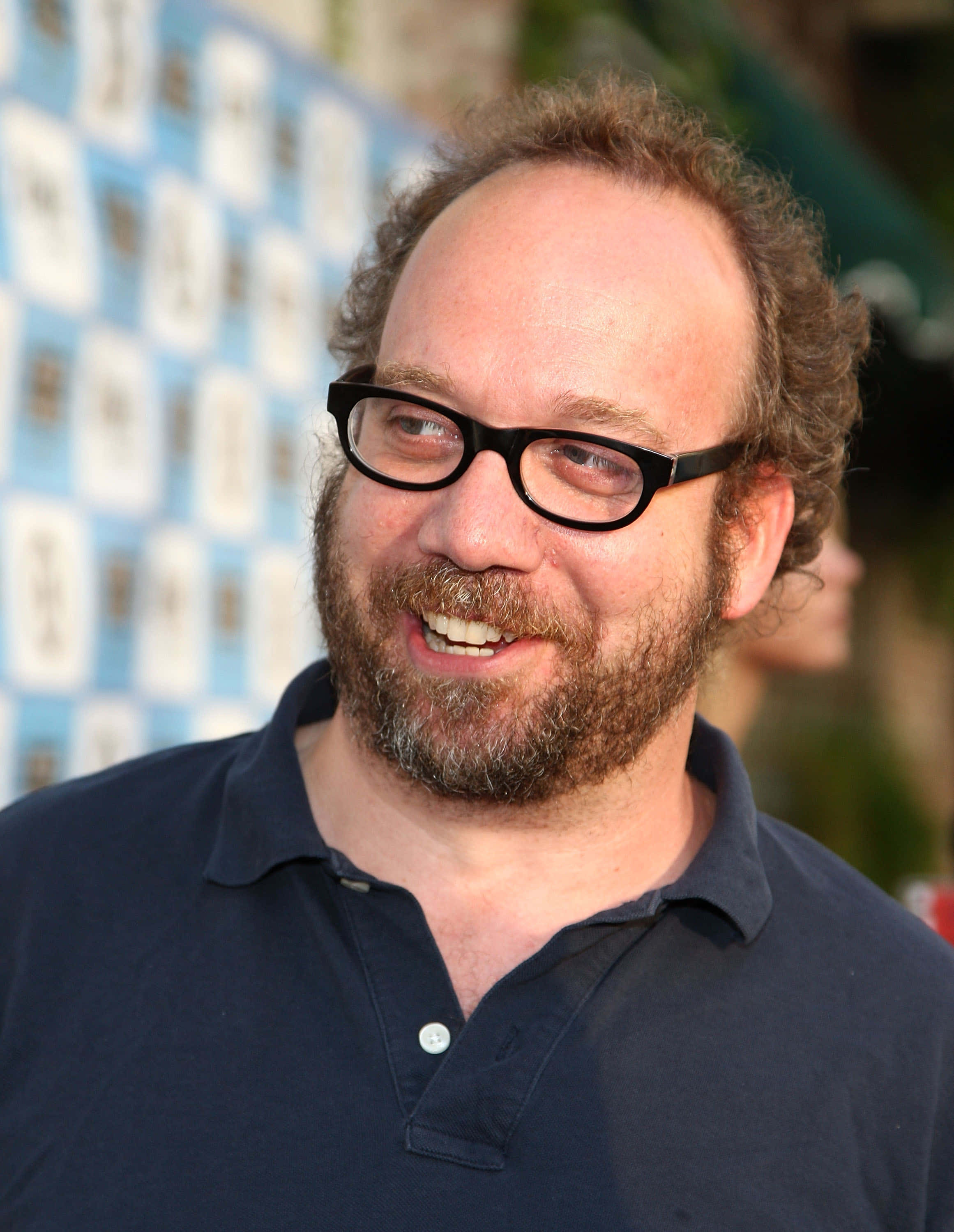 Paul Giamatti, dark polo shirt, blurred blue and white patterned backdrop, 2K Phone Wallpaper